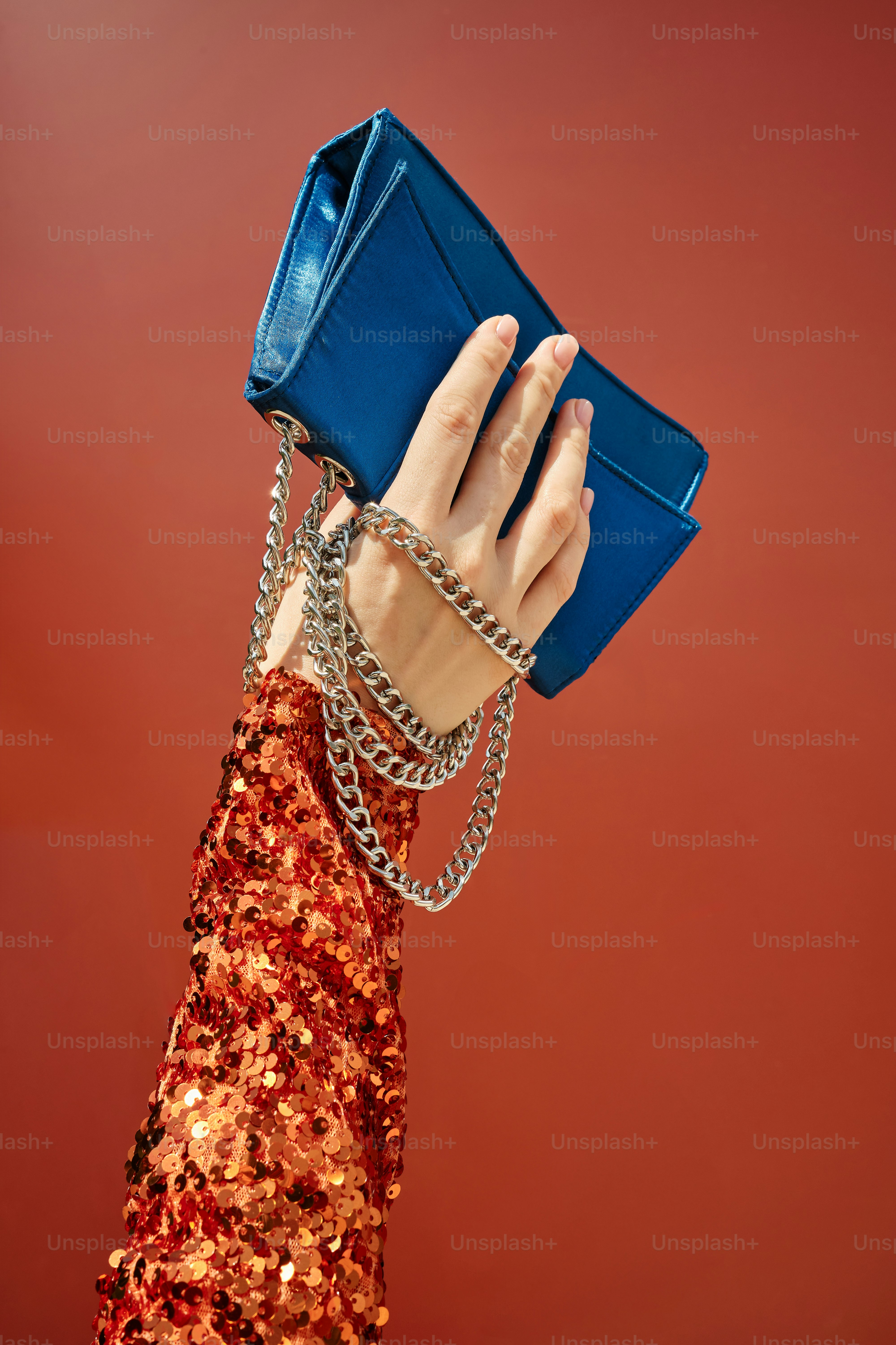 woman's hand in sequin blouse holding blue handbag on terracotta background