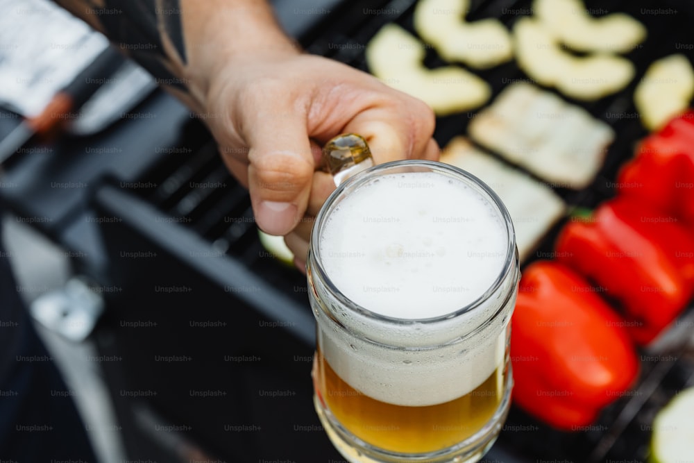 a person holding a glass of beer in front of a grill