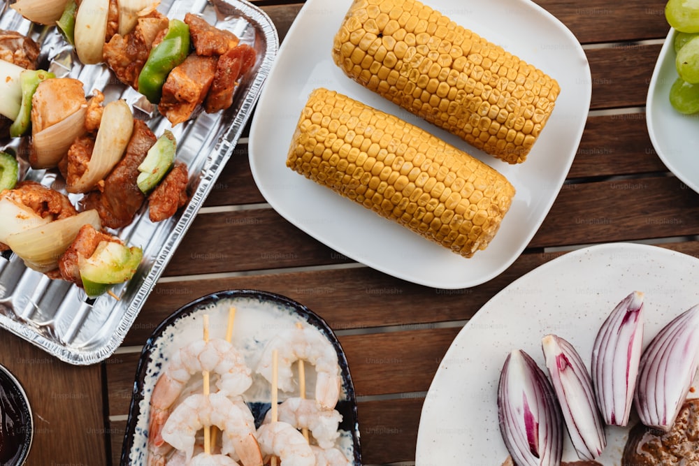 a table topped with plates of food and corn on the cob