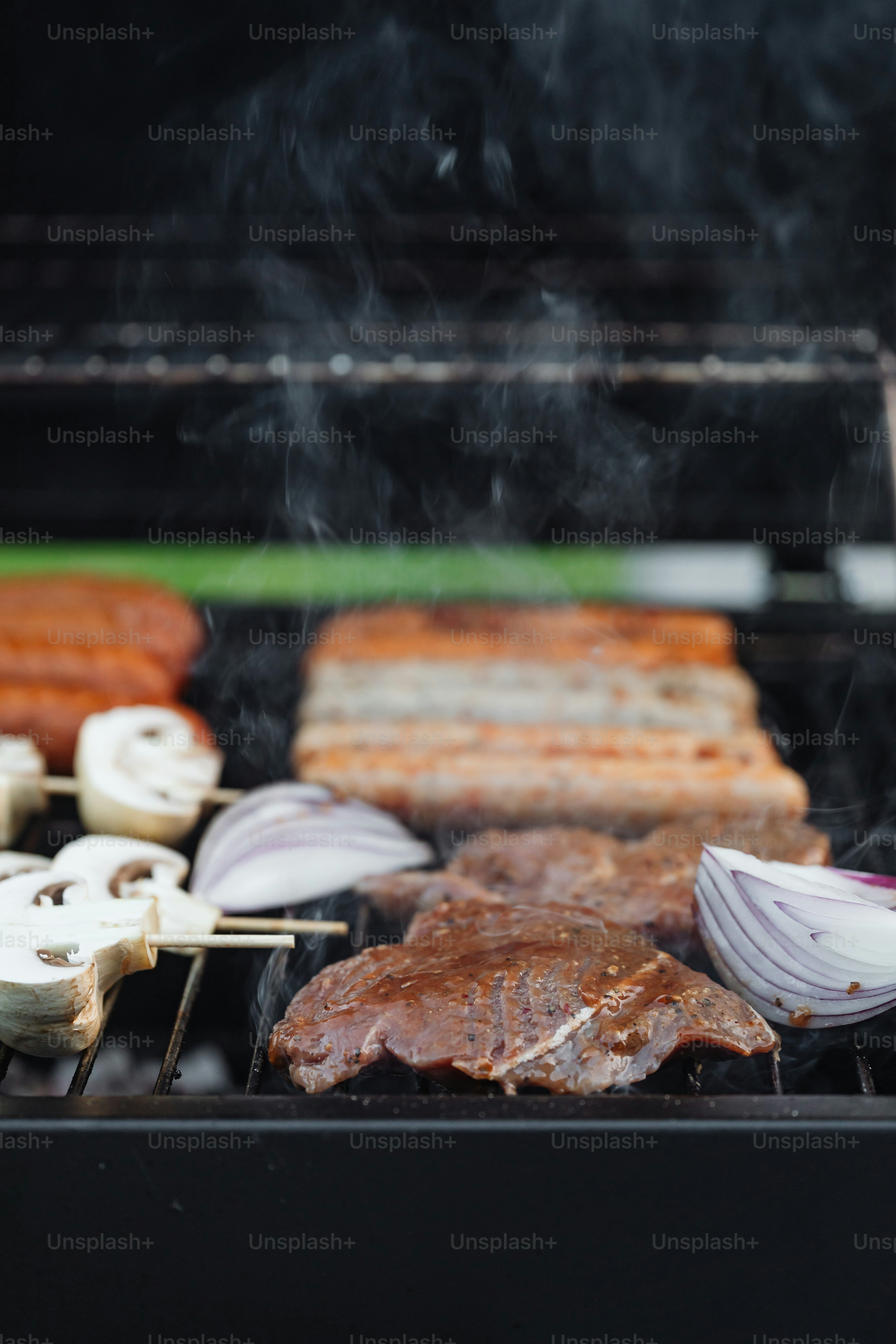 ein Grill mit Steaks, Zwiebeln und Pilzen, die darauf kochen