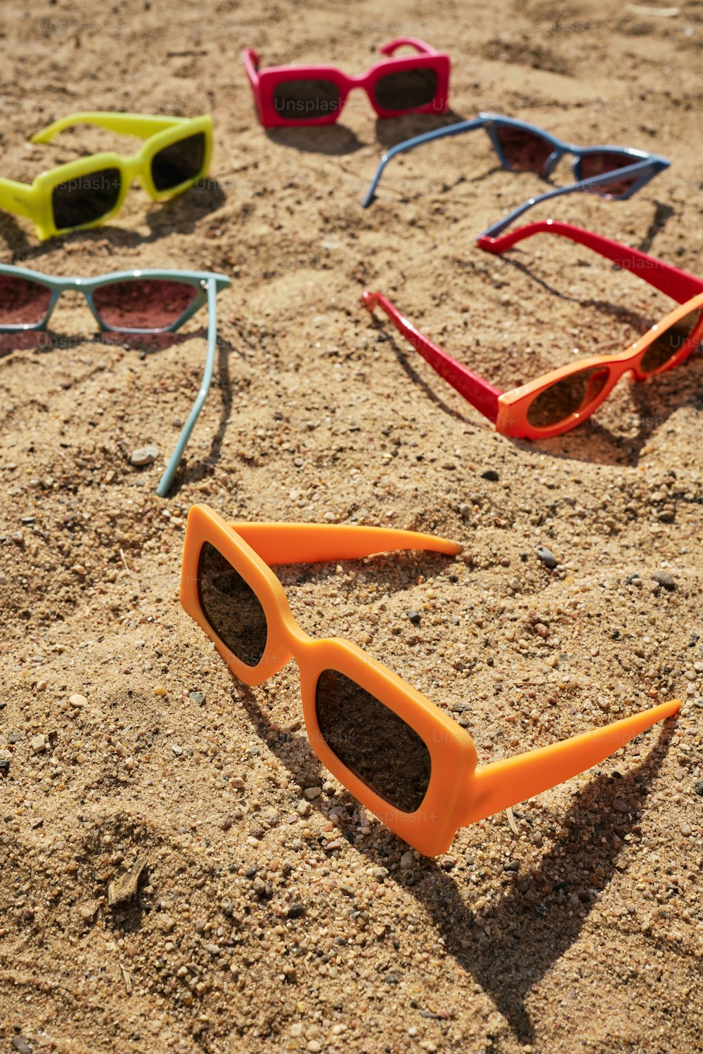 a group of sunglasses laying on top of a sandy beach