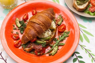 an orange plate topped with a croissant sandwich