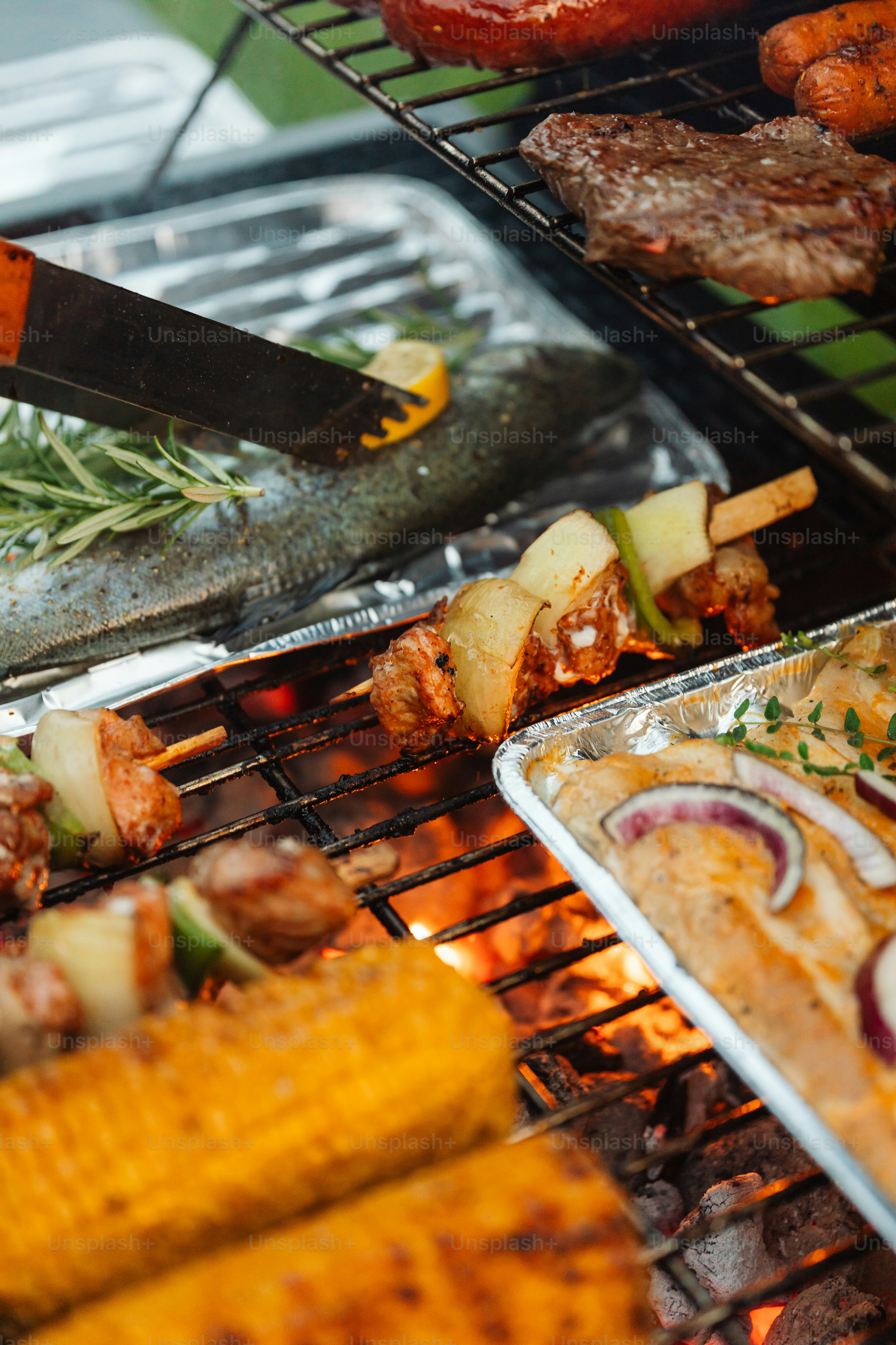 a bbq grill with meat, vegetables and corn on the cob