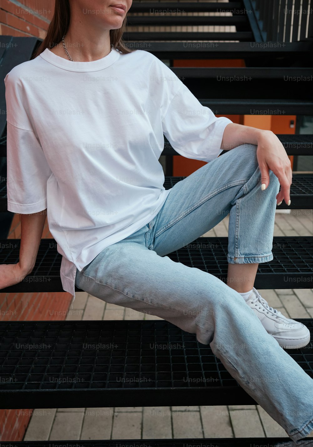 a woman sitting on a set of stairs wearing a white shirt and jeans