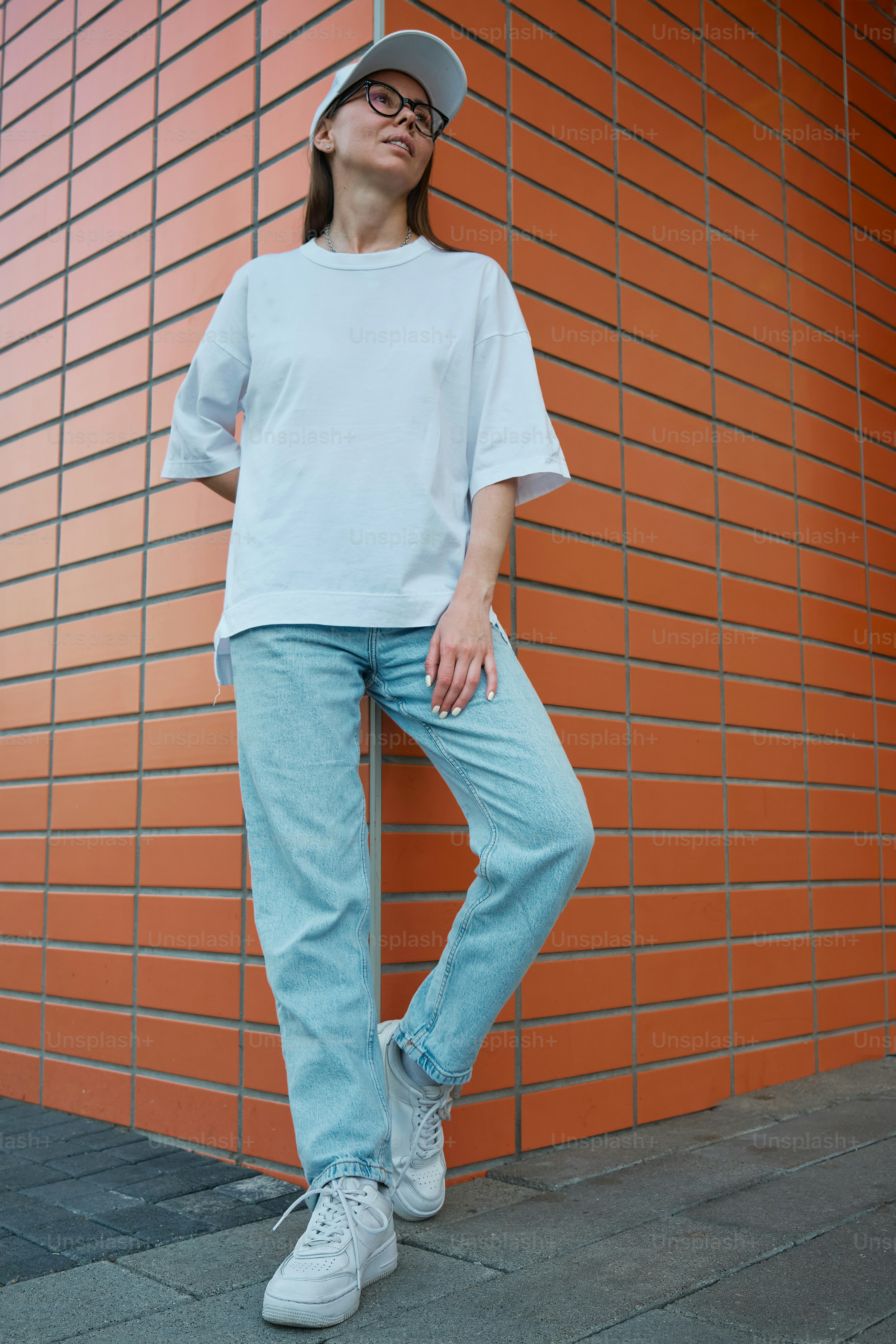 レンガの壁に手を当てて腰に立つ女性