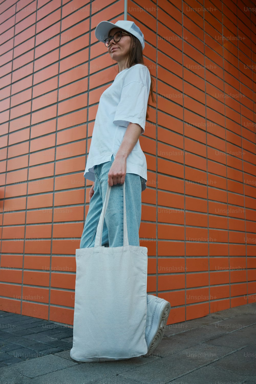 a woman holding a white bag standing in front of a brick wall