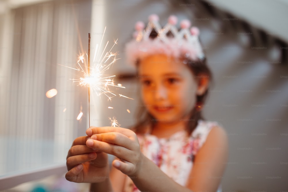a little girl wearing a tiara holding a sparkler