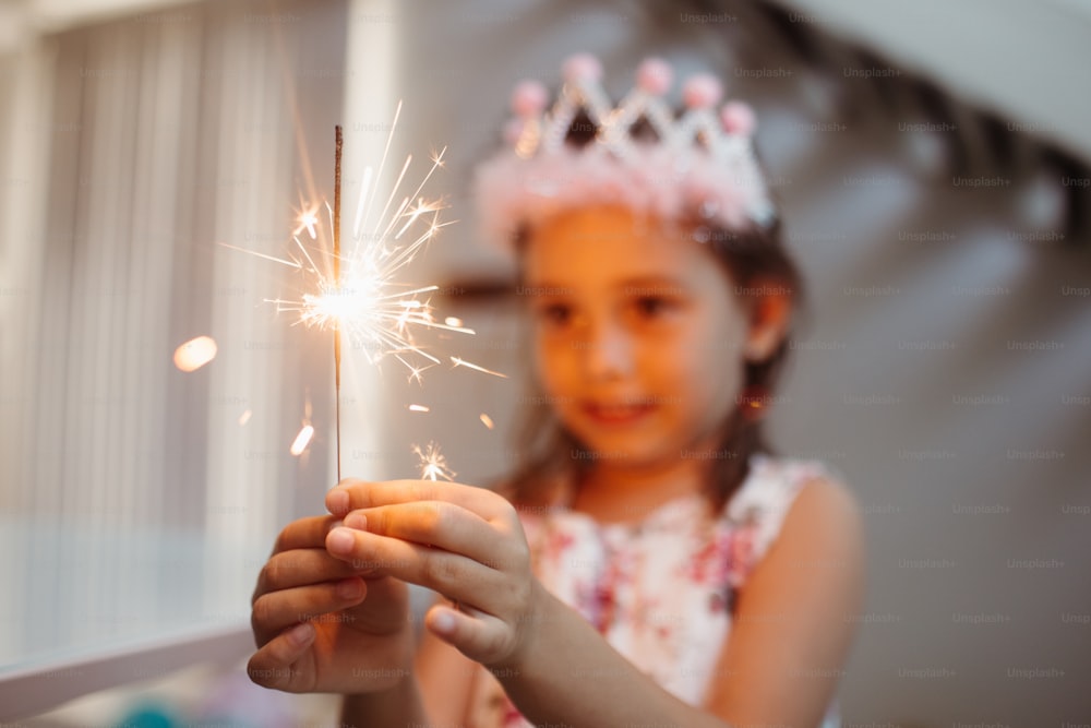 Ein kleines Mädchen, das ein Diadem trägt und eine Wunderkerze hält