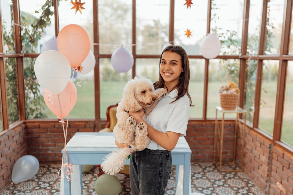 a woman holding a dog in a room with balloons