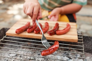 a person is cutting up some hot dogs on a grill