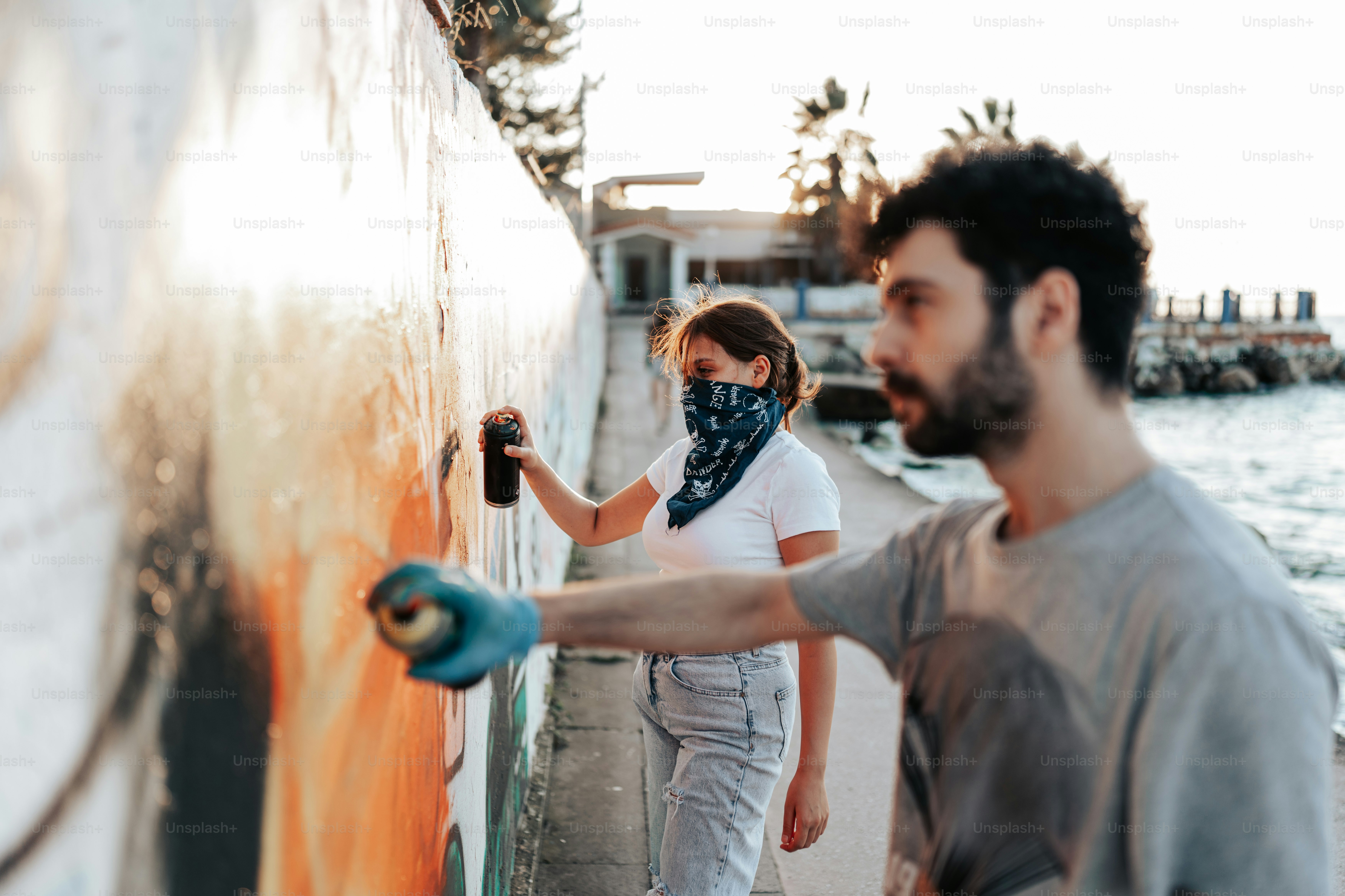 A man painting a wall with orange spray paint photo – Graffiti Image on ...