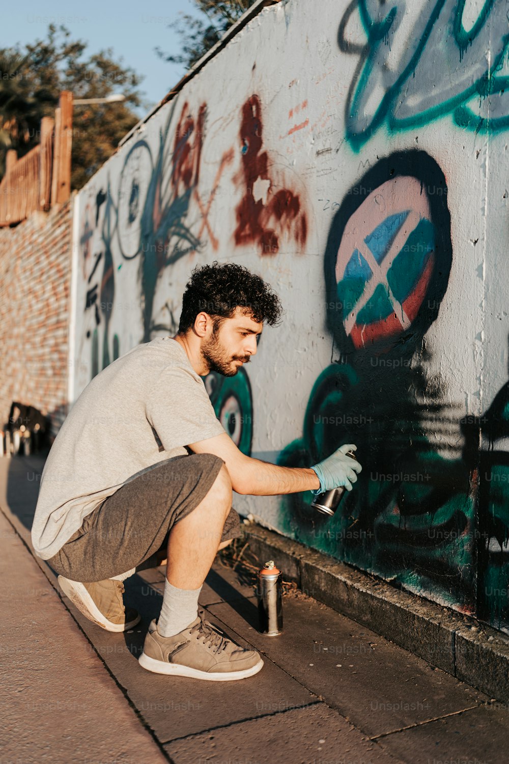 a man kneeling down next to a wall with graffiti on it