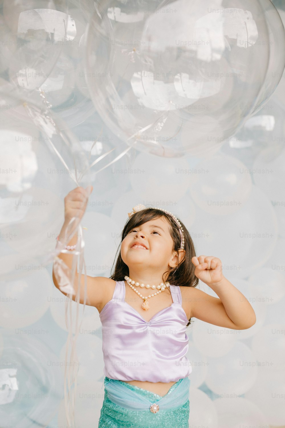 a little girl holding a bunch of clear balloons