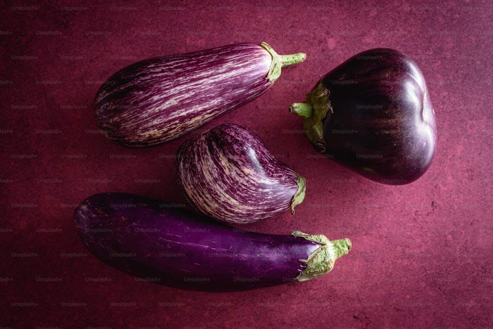 three eggplant and two eggplant on a red surface