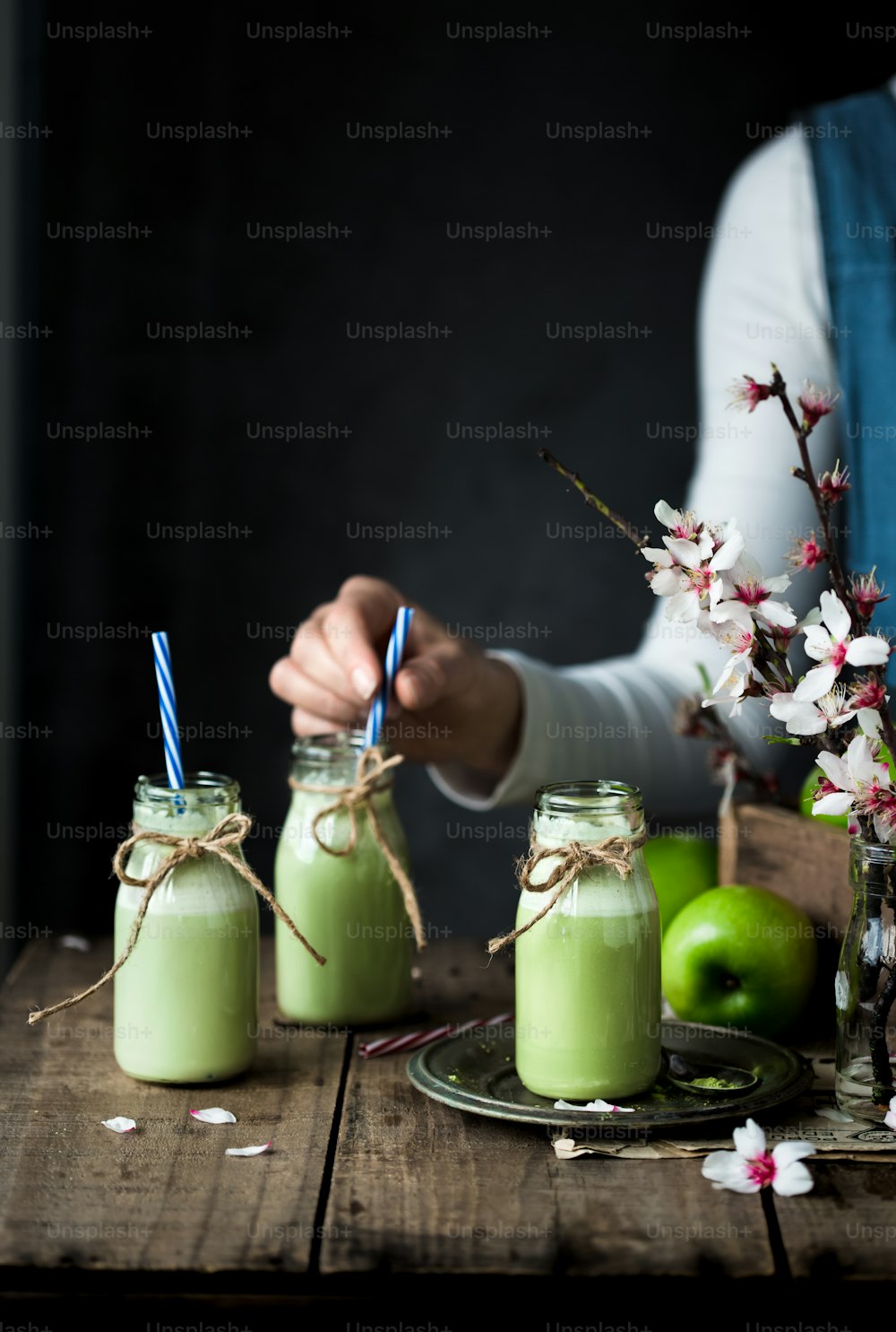 a person holding a straw in front of three jars filled with green liquid