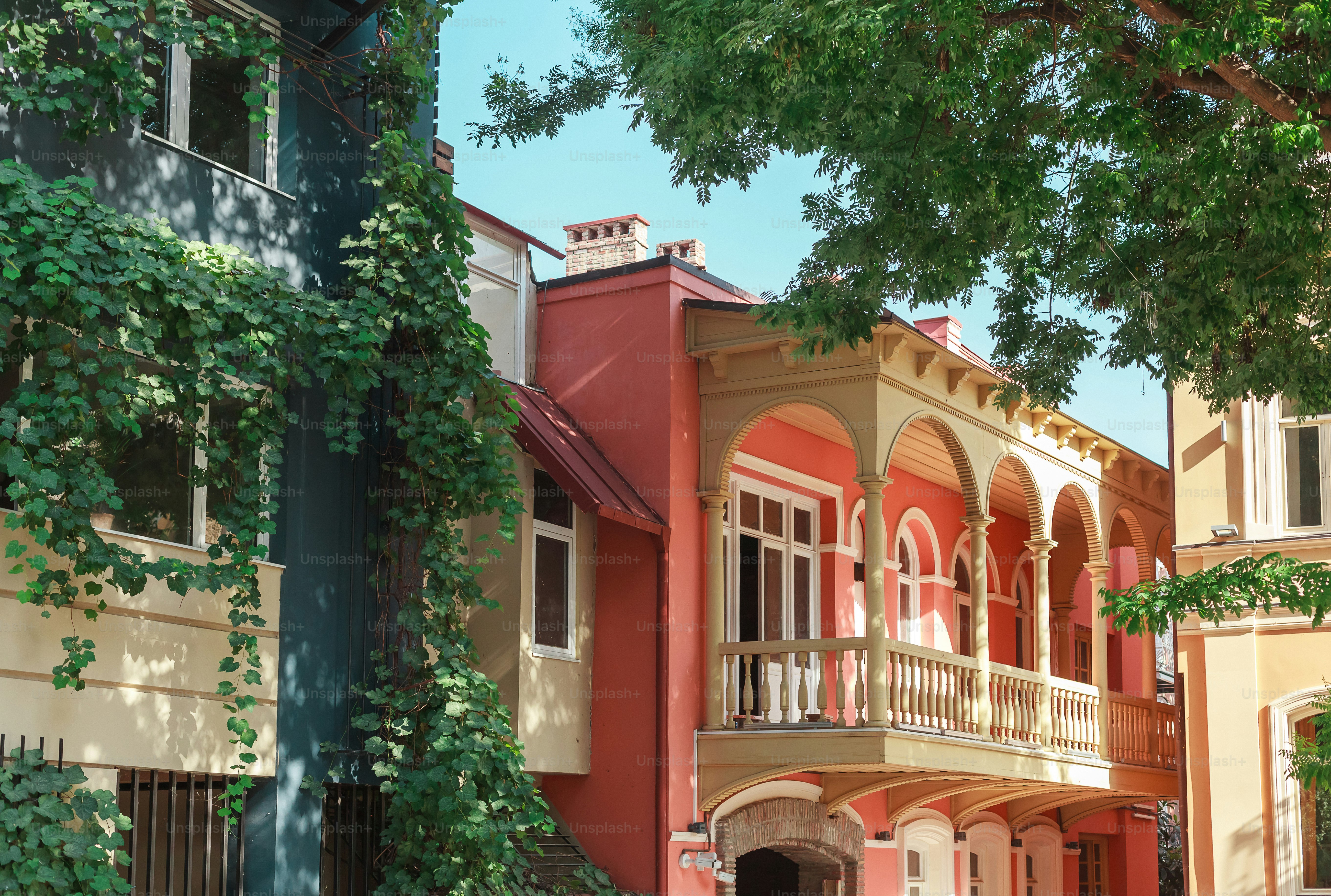 a red building with a balcony and a green tree