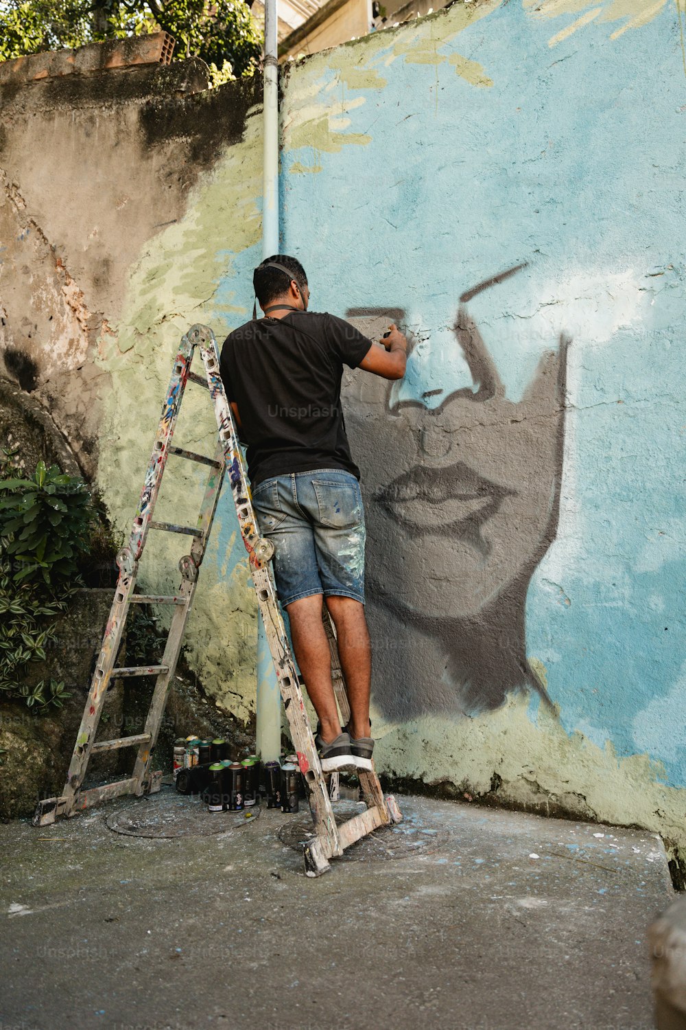 Ein Mann auf einer Leiter, der ein Wandbild an eine Wand malt