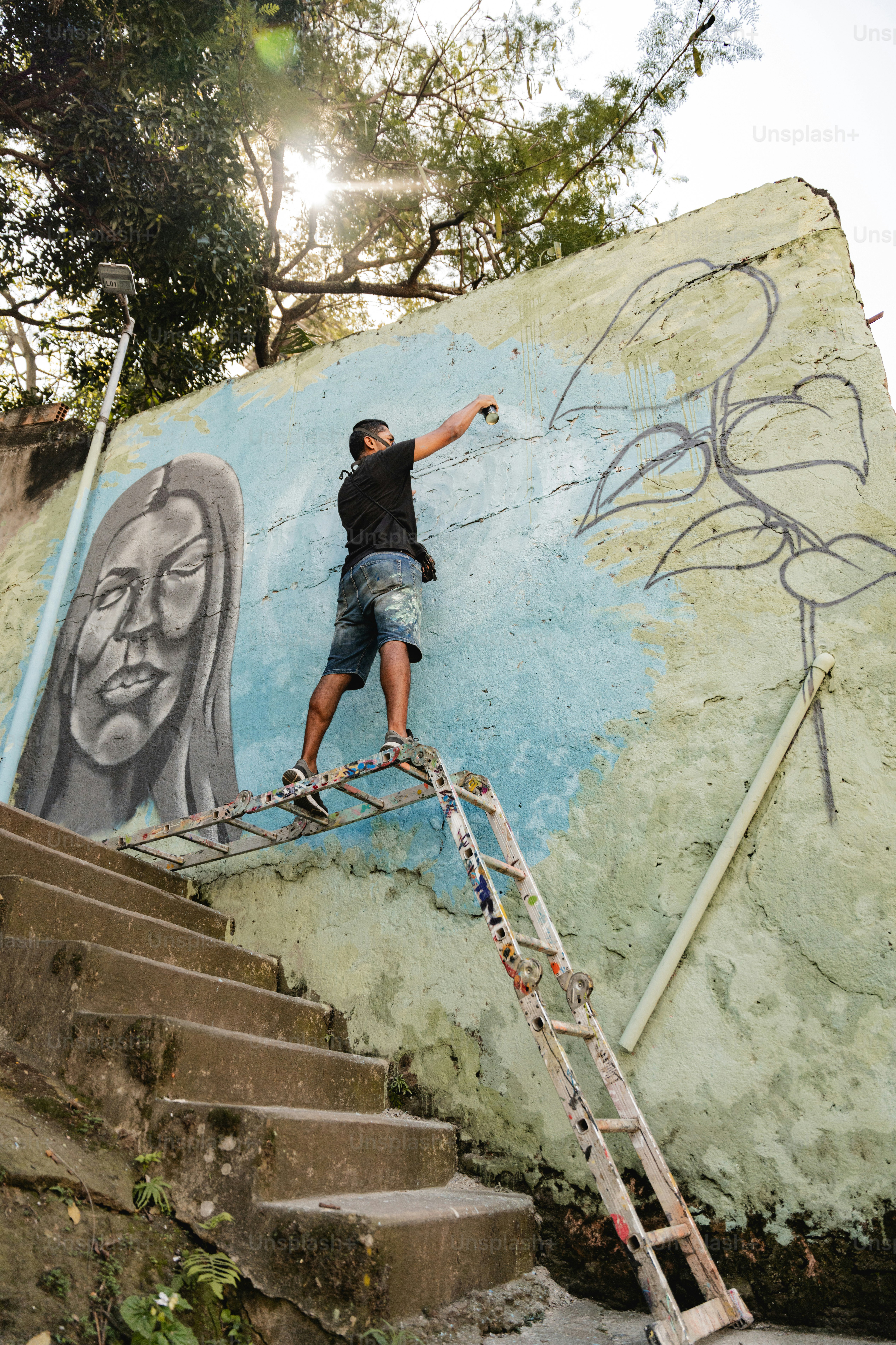 A man painting a mural on the side of a building photo – Graffiti Image ...