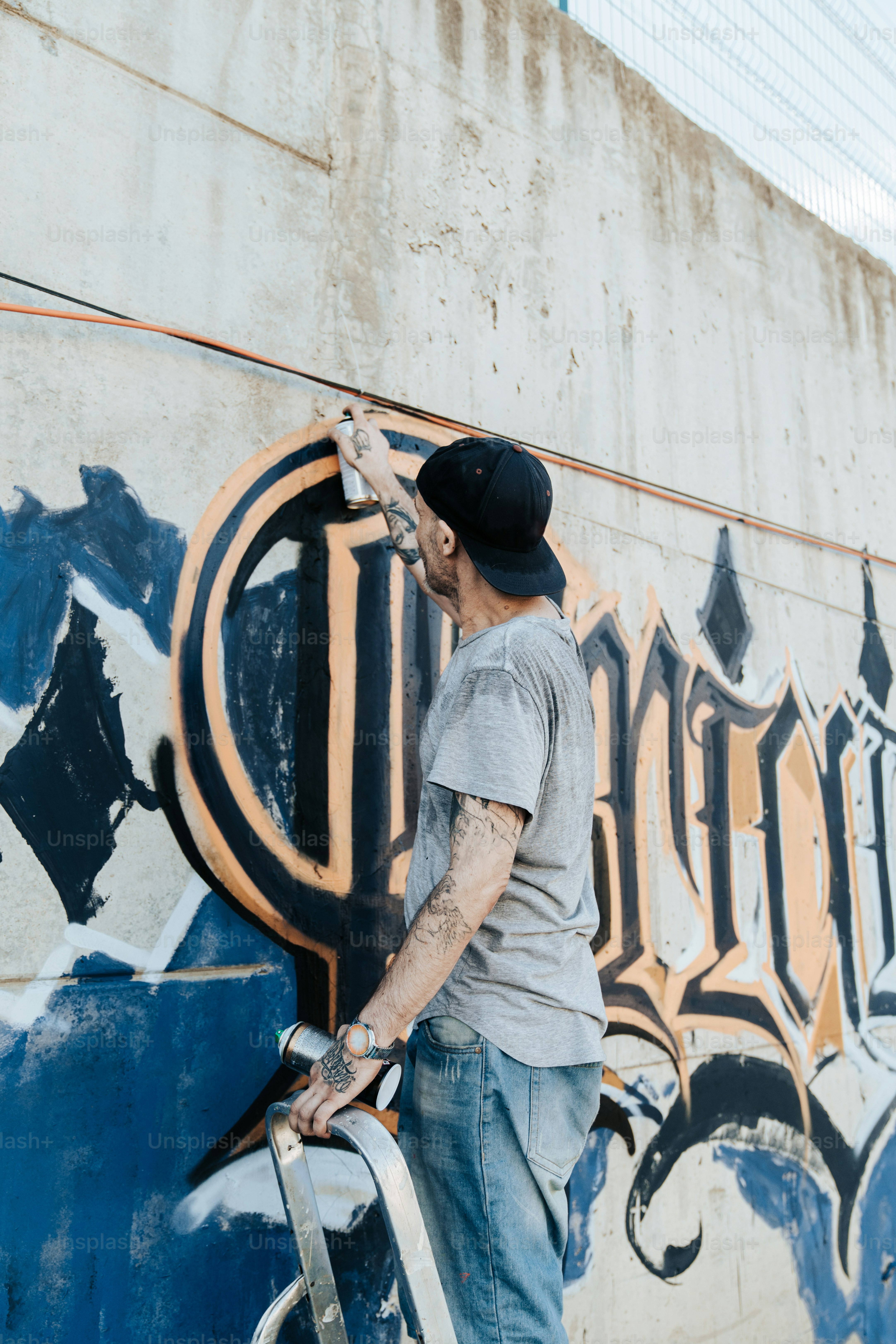 Un hombre está pintando una pared con graffiti foto – Imagen de ...