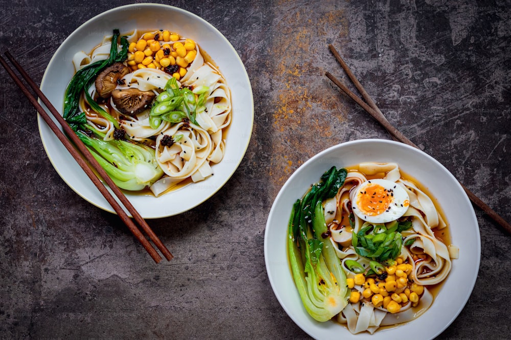 two bowls of noodles and vegetables with chopsticks