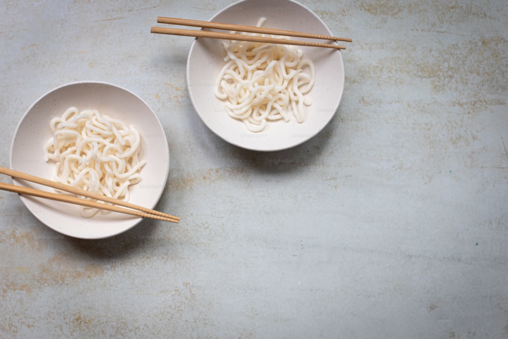 two bowls of noodles with chopsticks on a table