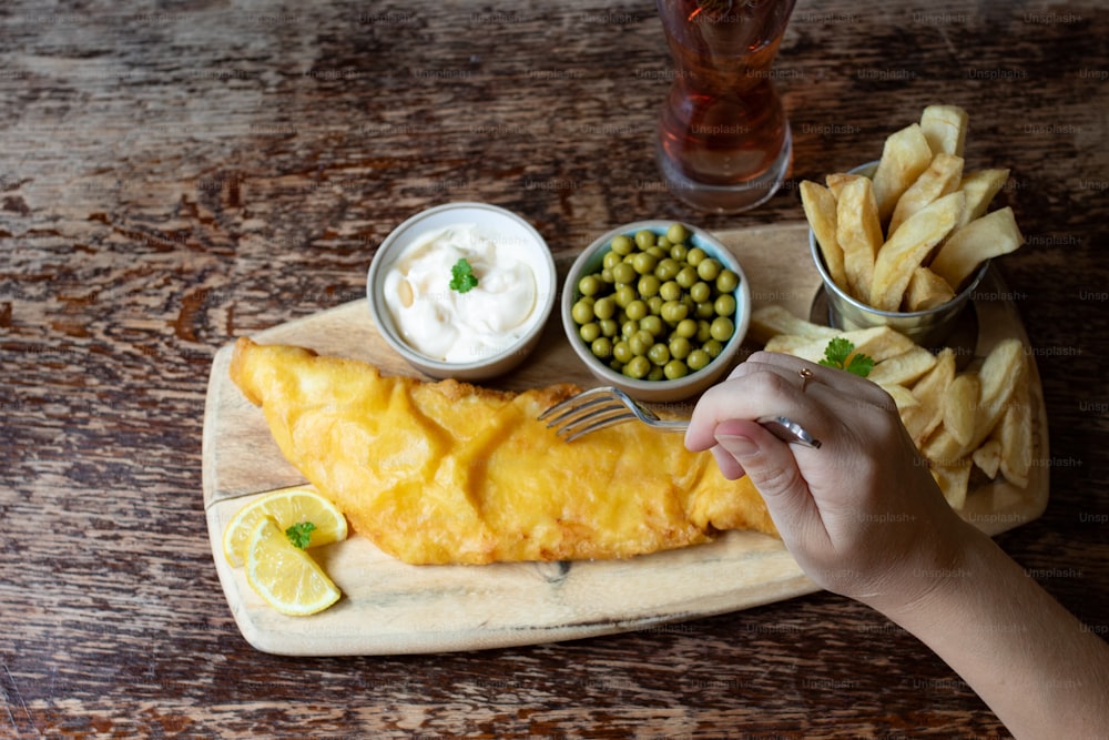 a person holding a fork over a fish and chips