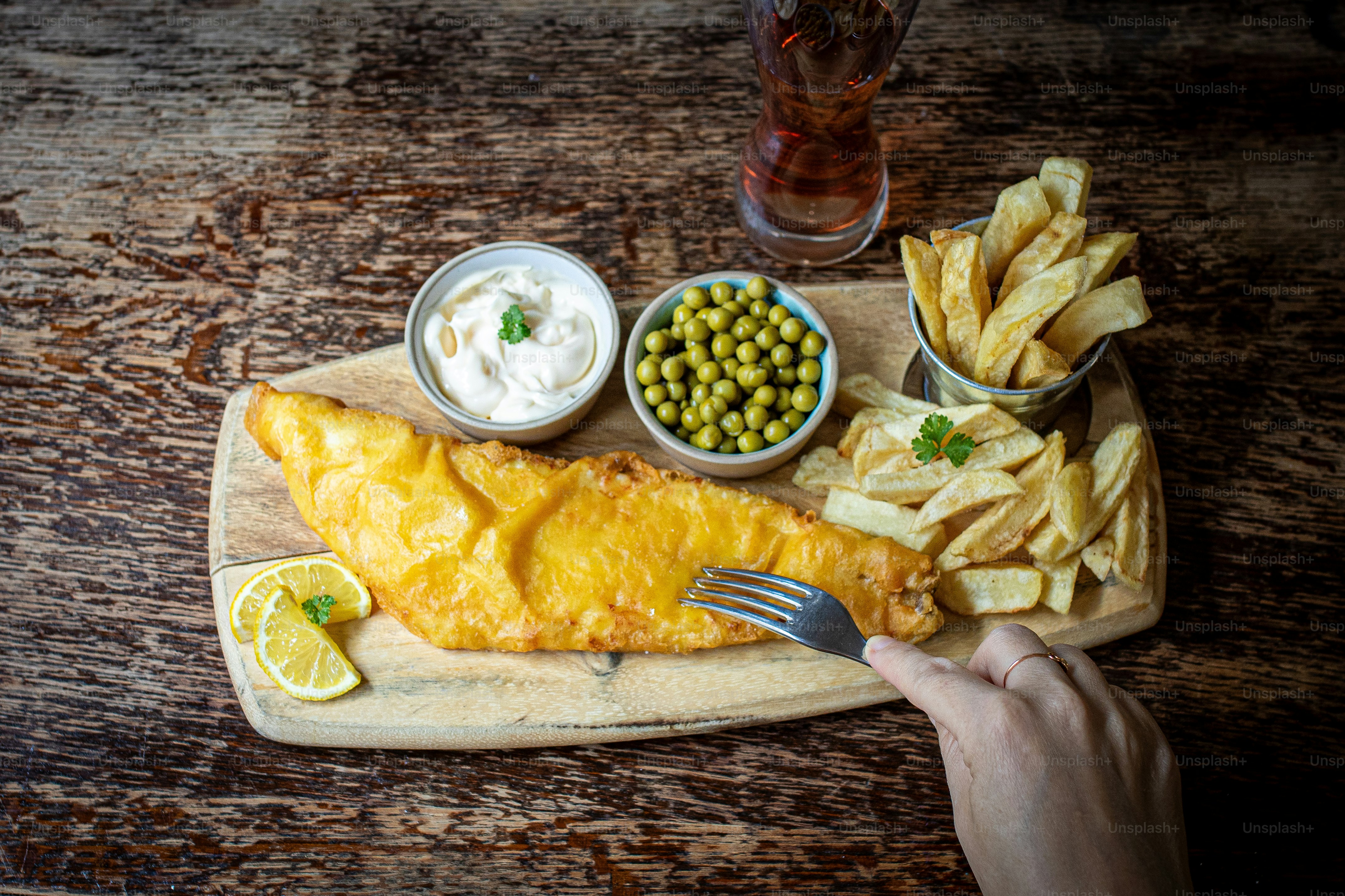 a person holding a fork near a fish and chips