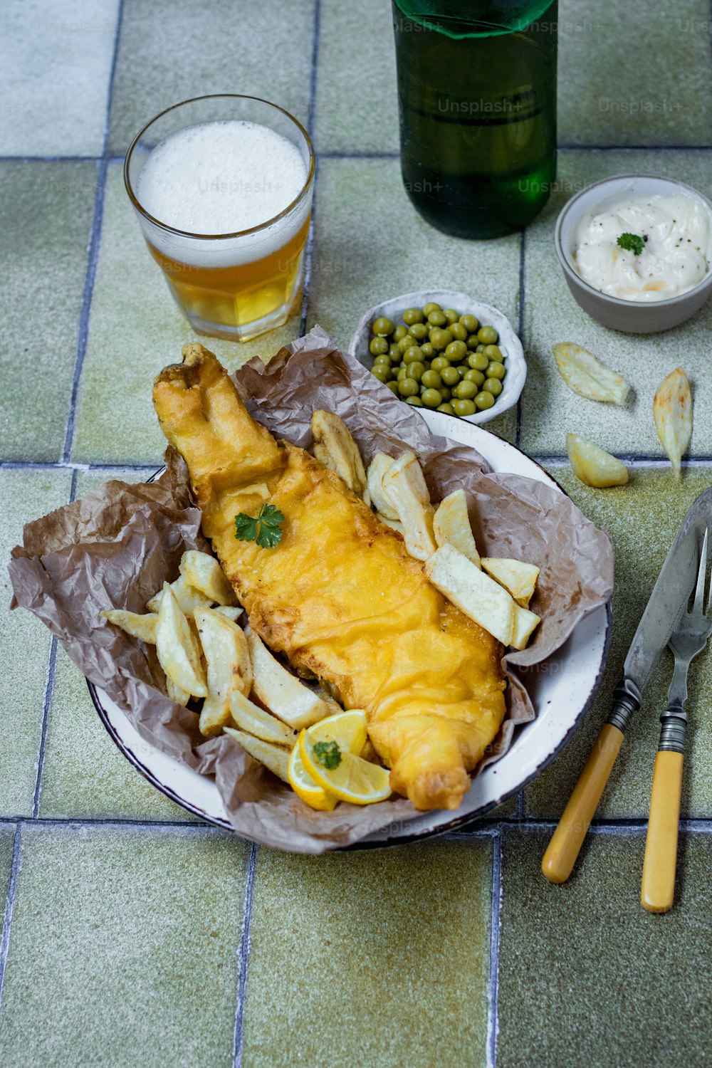 um prato de peixe e batatas fritas ao lado de um copo de cerveja