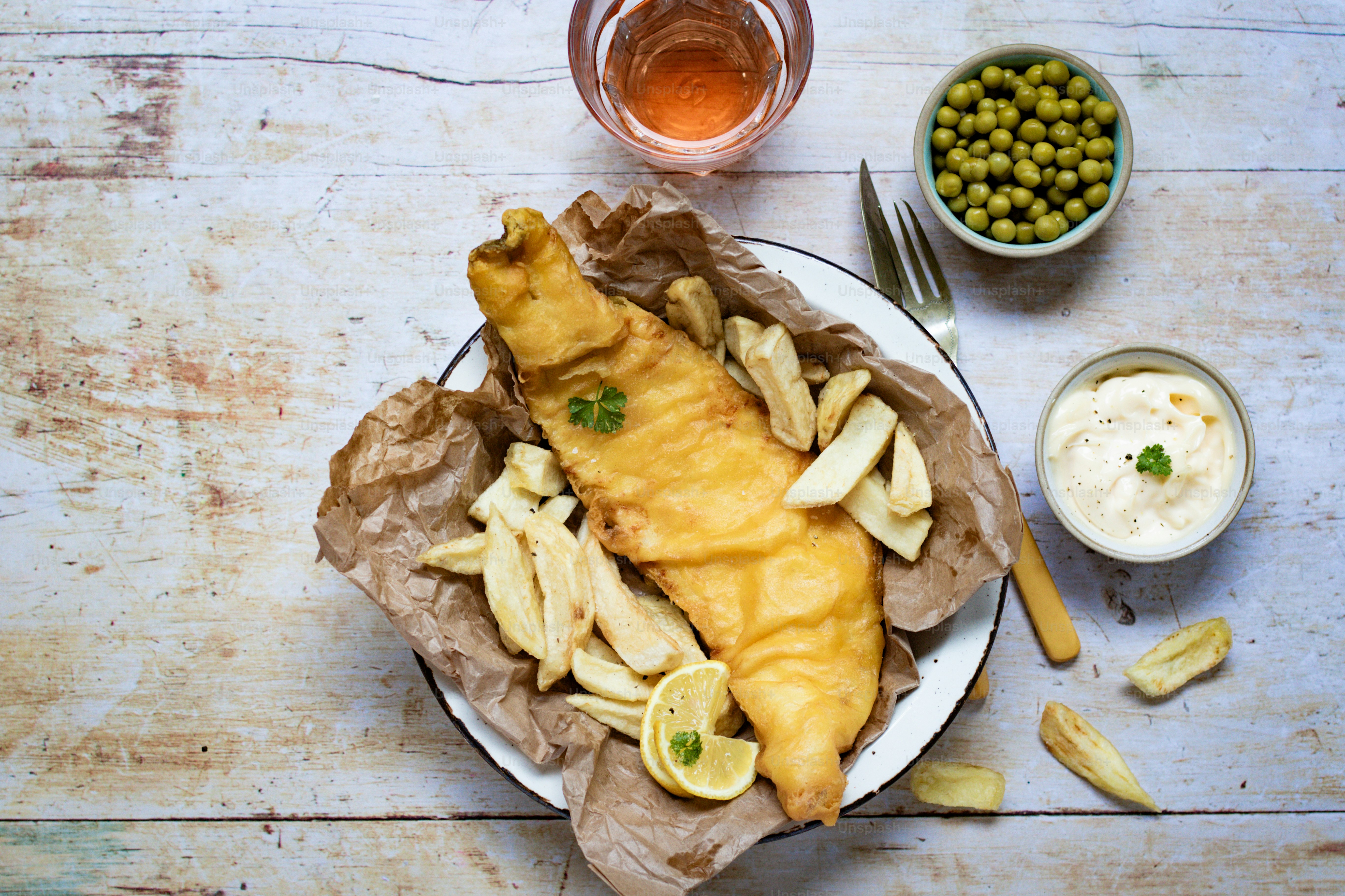 a plate of fish and chips with a side of peas