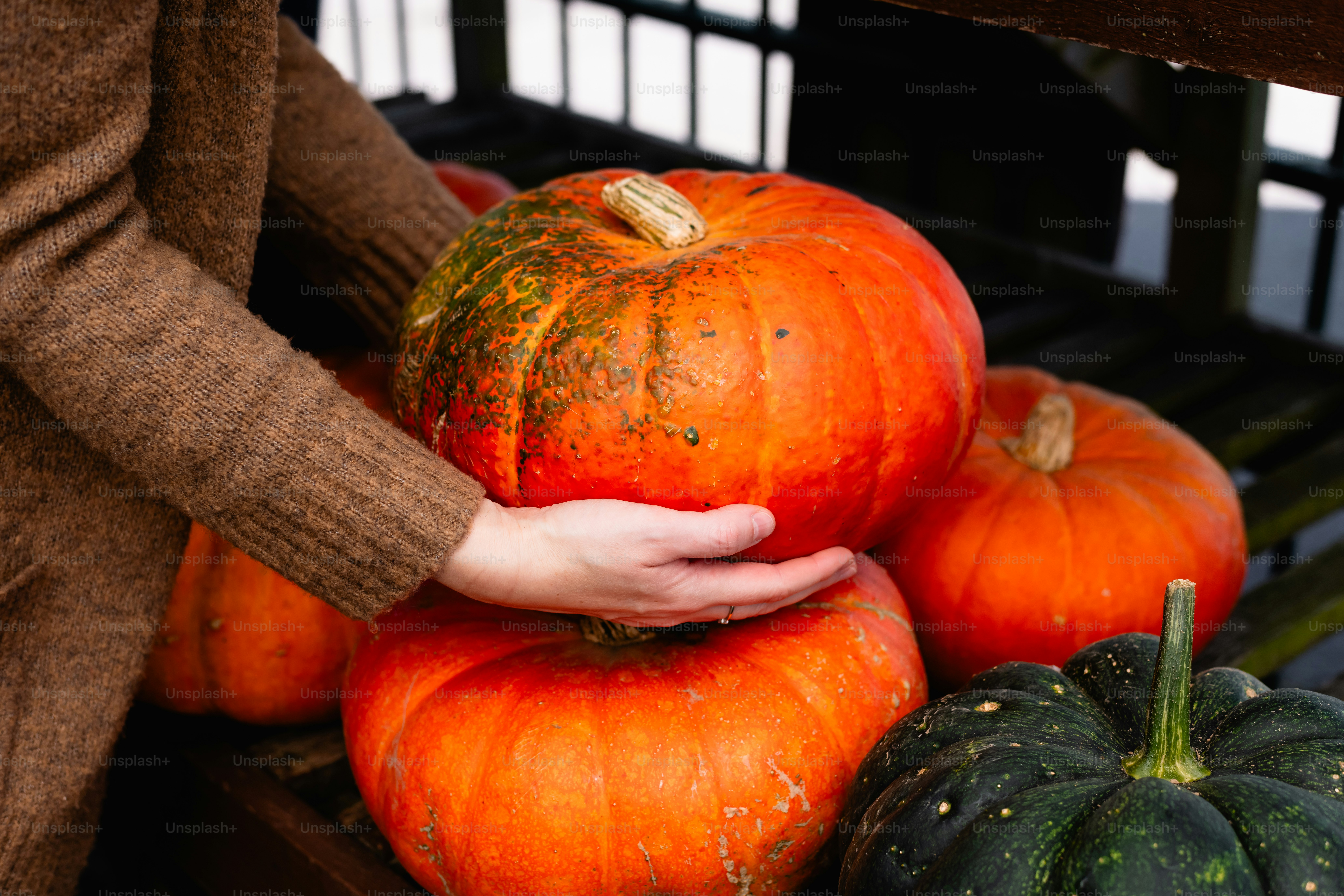 a person holding a pumpkin in front of a pile of pumpkins