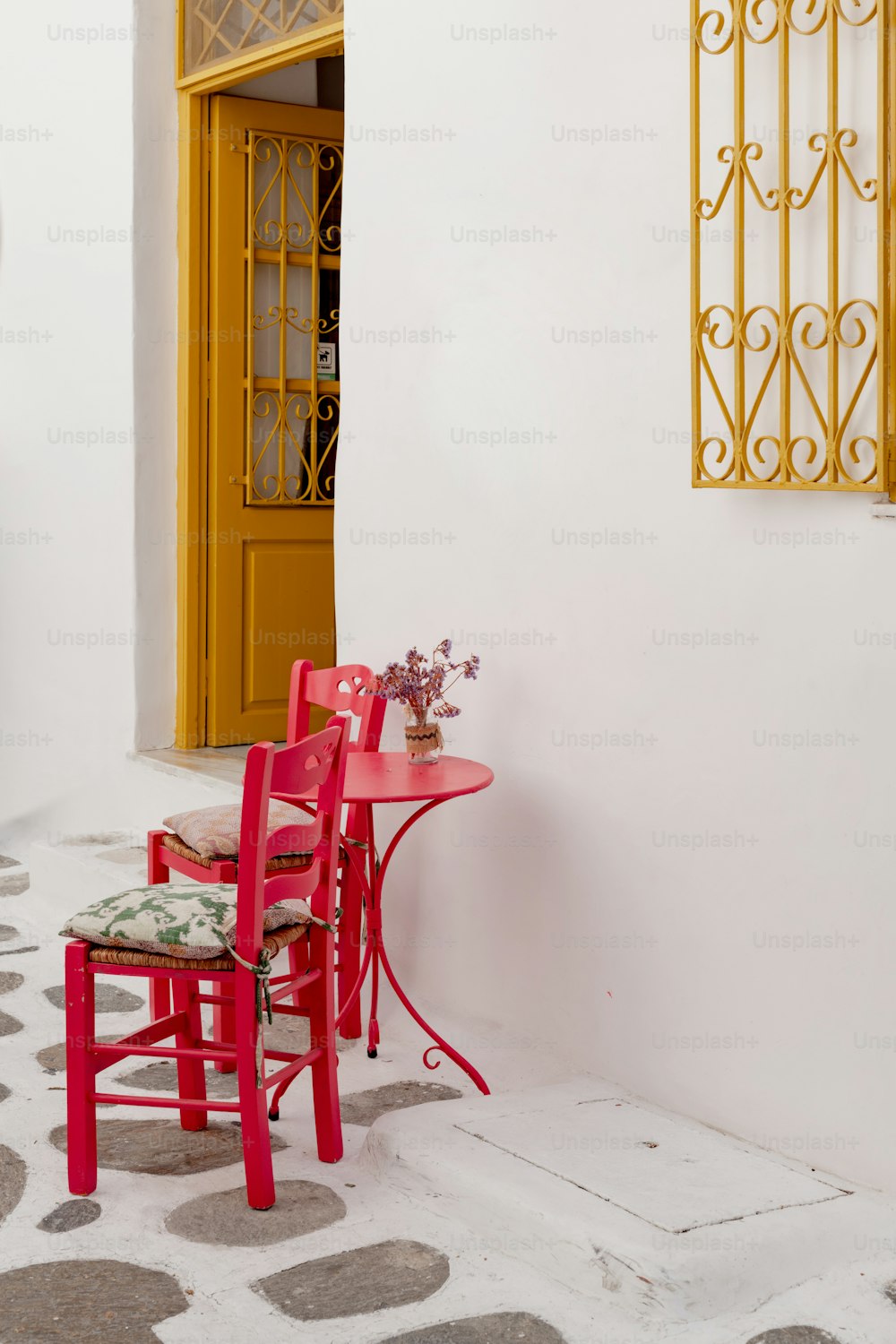 a red table and two red chairs in front of a yellow door