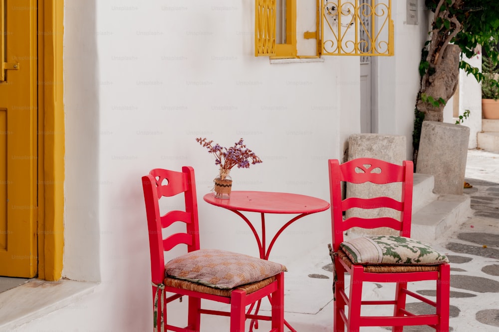 two red chairs and a table with a vase of flowers on it