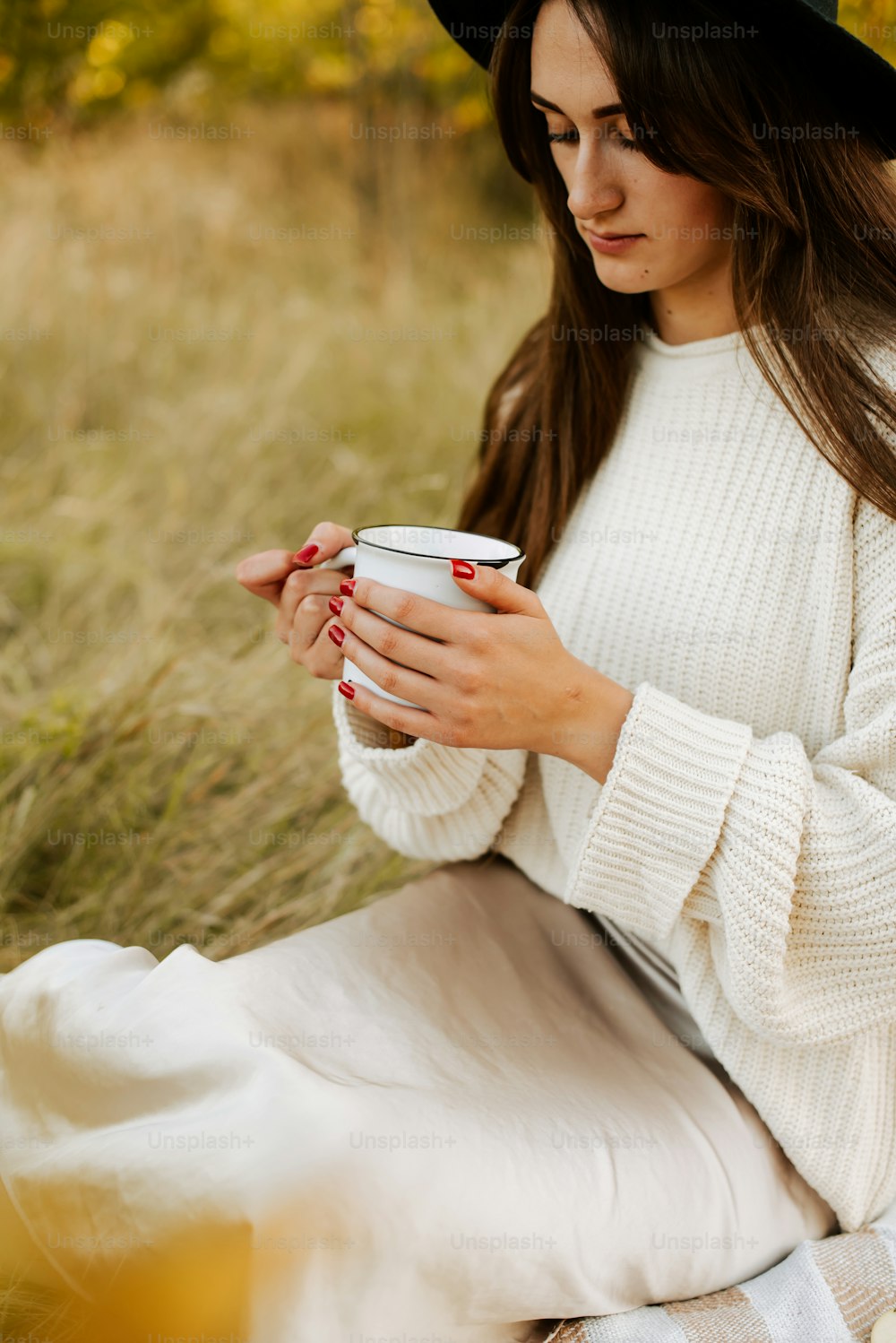 a woman sitting on a blanket holding a cup of coffee