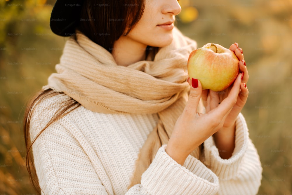 a woman in a hat and scarf holding an apple