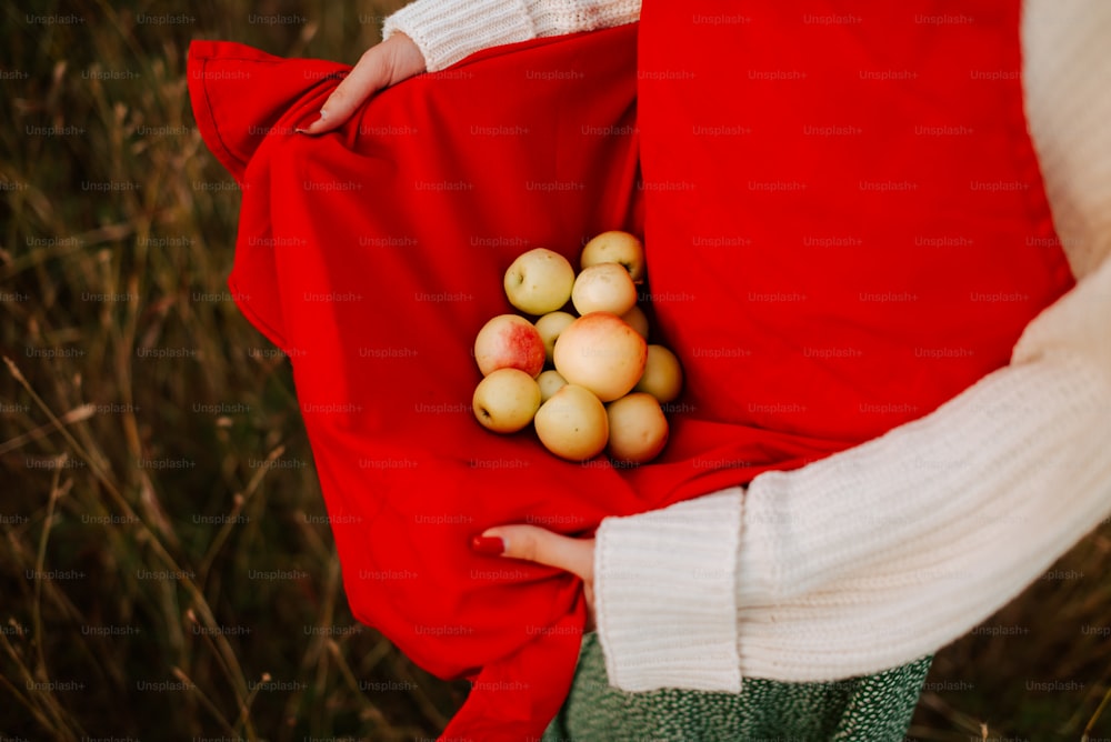 a woman in a red vest holding a bunch of apples