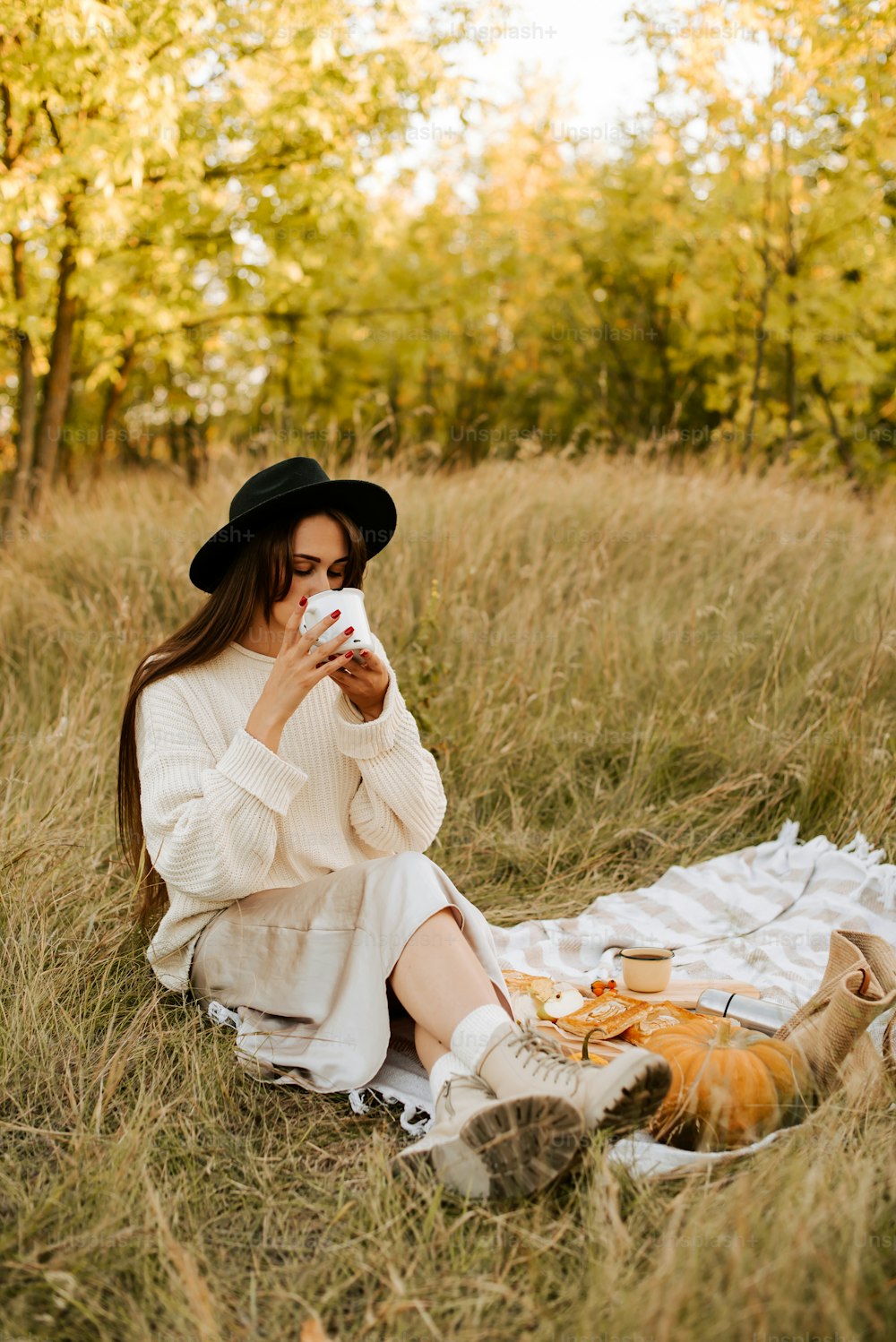 a woman sitting in a field drinking a cup of coffee