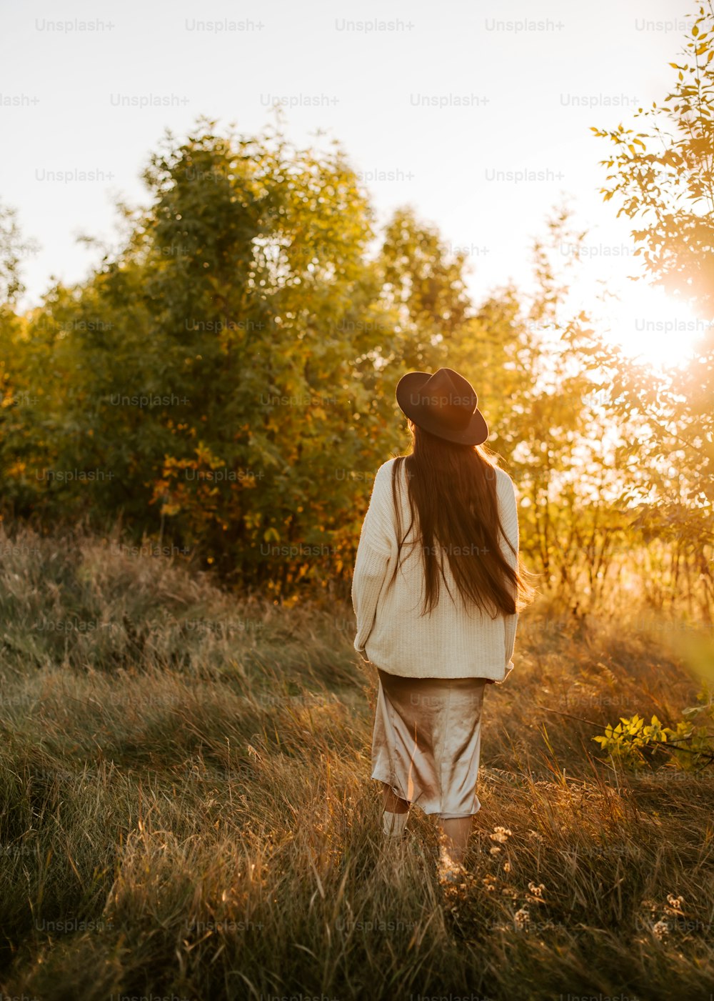 a woman with long hair walking through a field