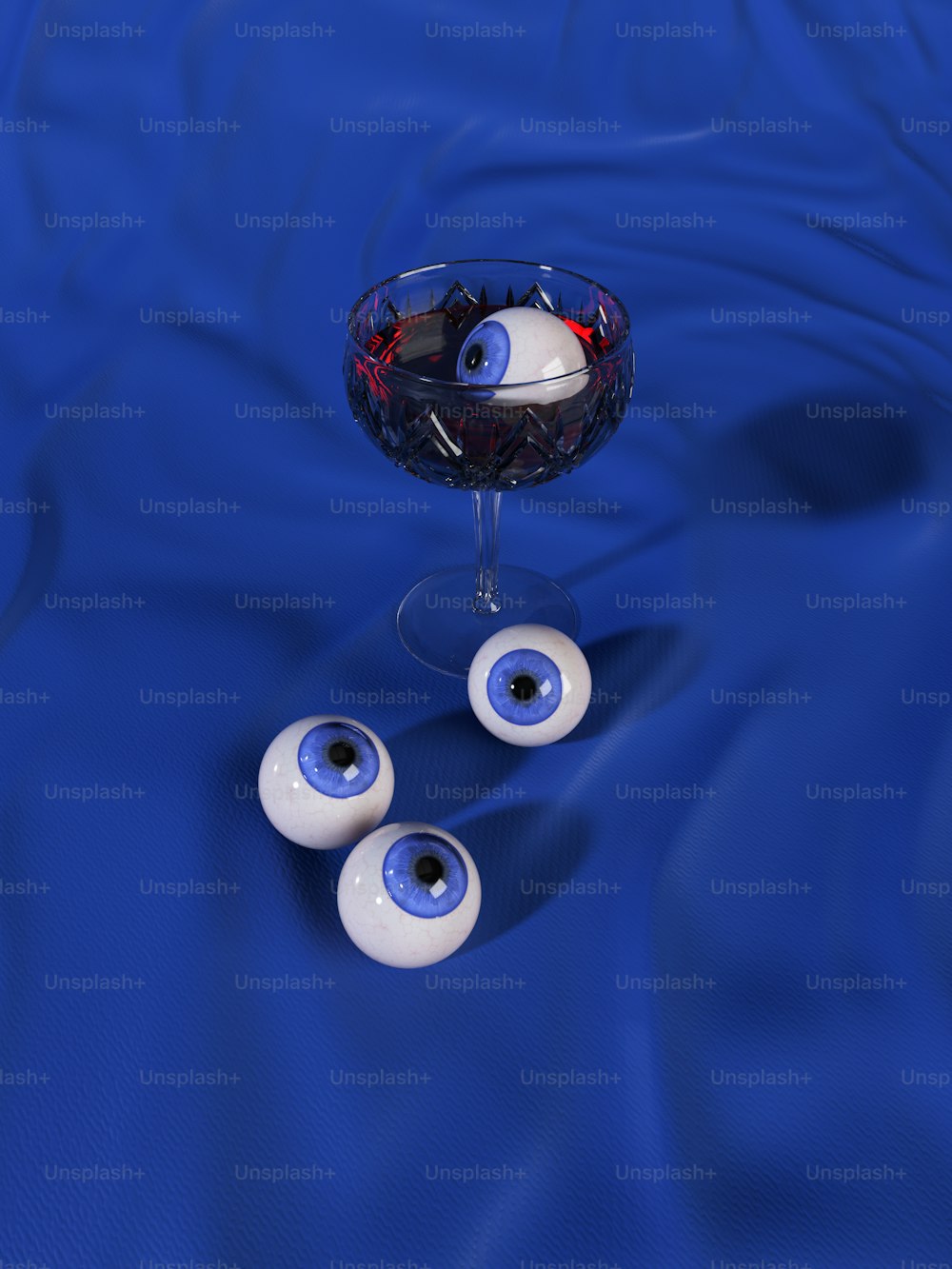 um copo de vinho e três maus olhos em uma superfície azul