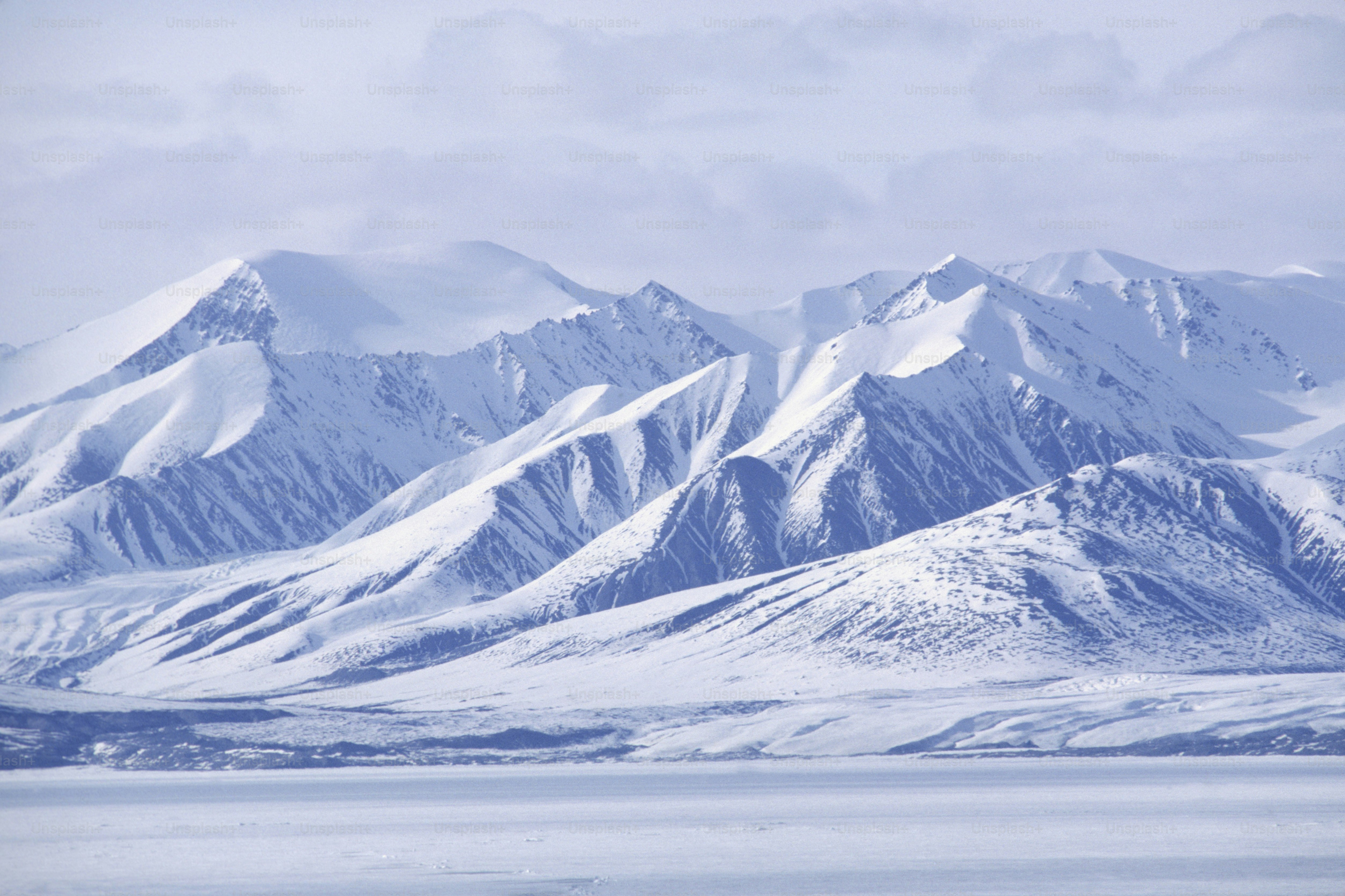 a mountain range covered in snow under a cloudy sky