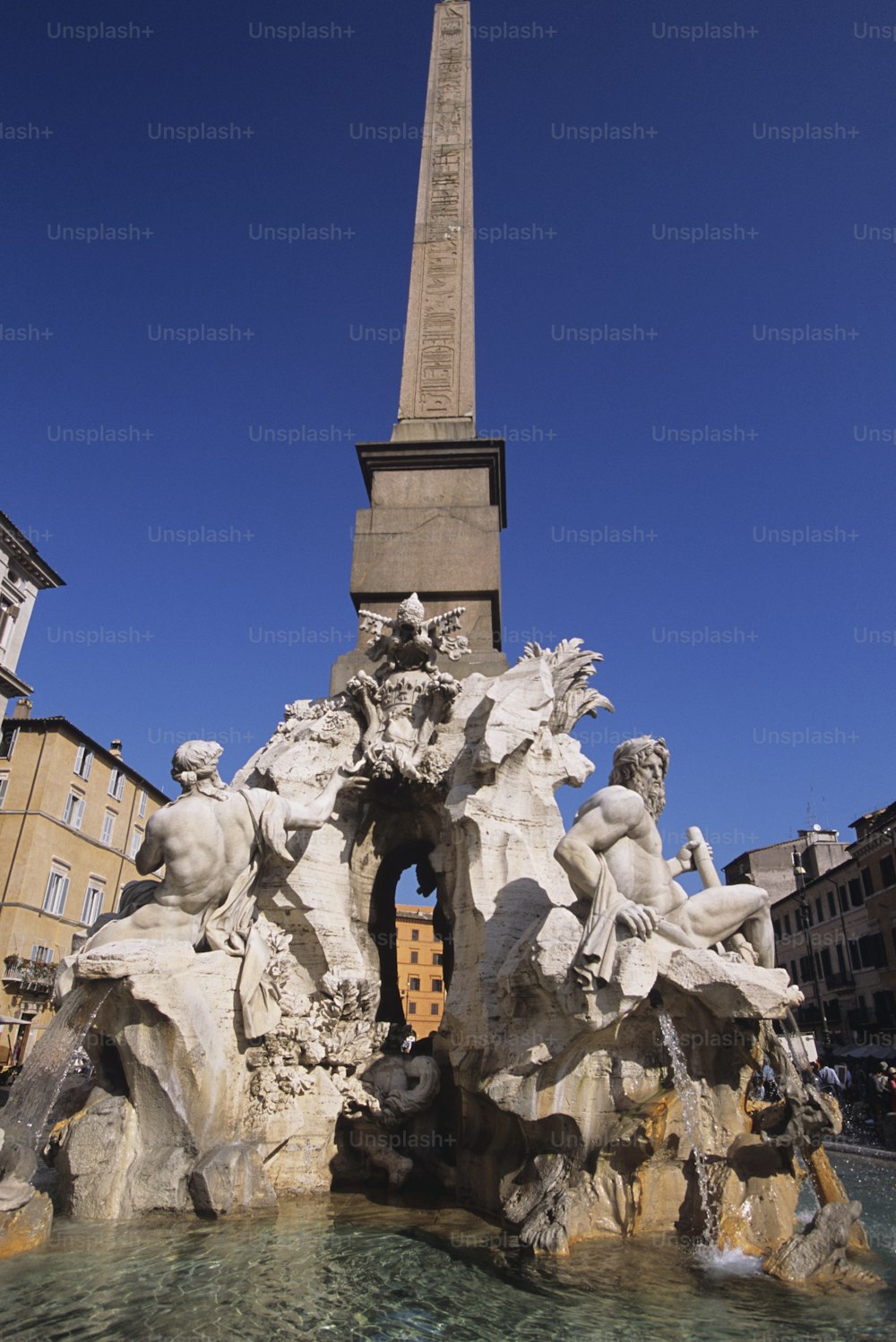 Una fuente con estatuas frente a un alto obelisco