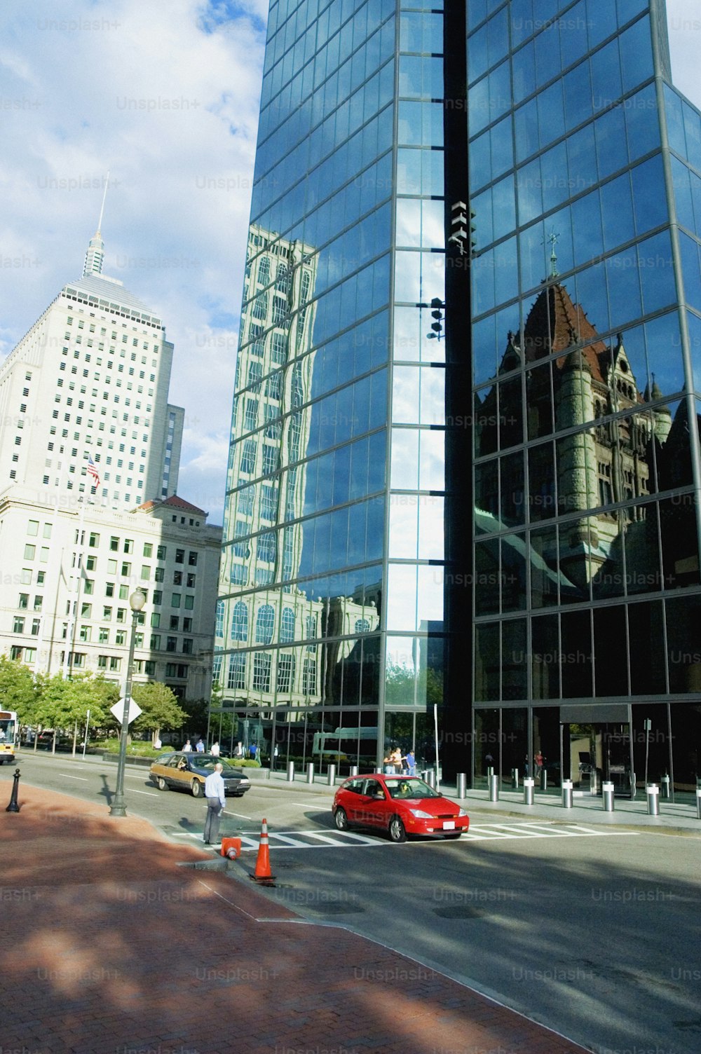 a red car driving past a tall glass building