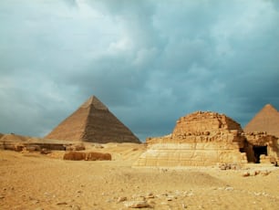 a group of pyramids in the desert under a cloudy sky