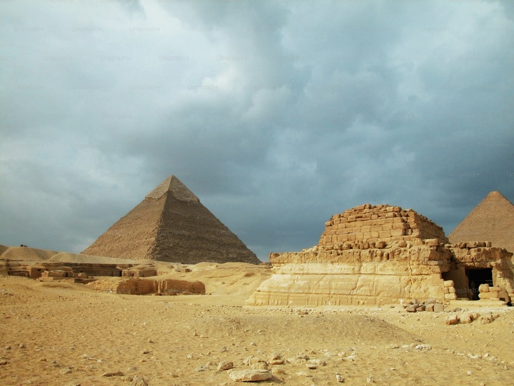 a group of pyramids in the desert under a cloudy sky