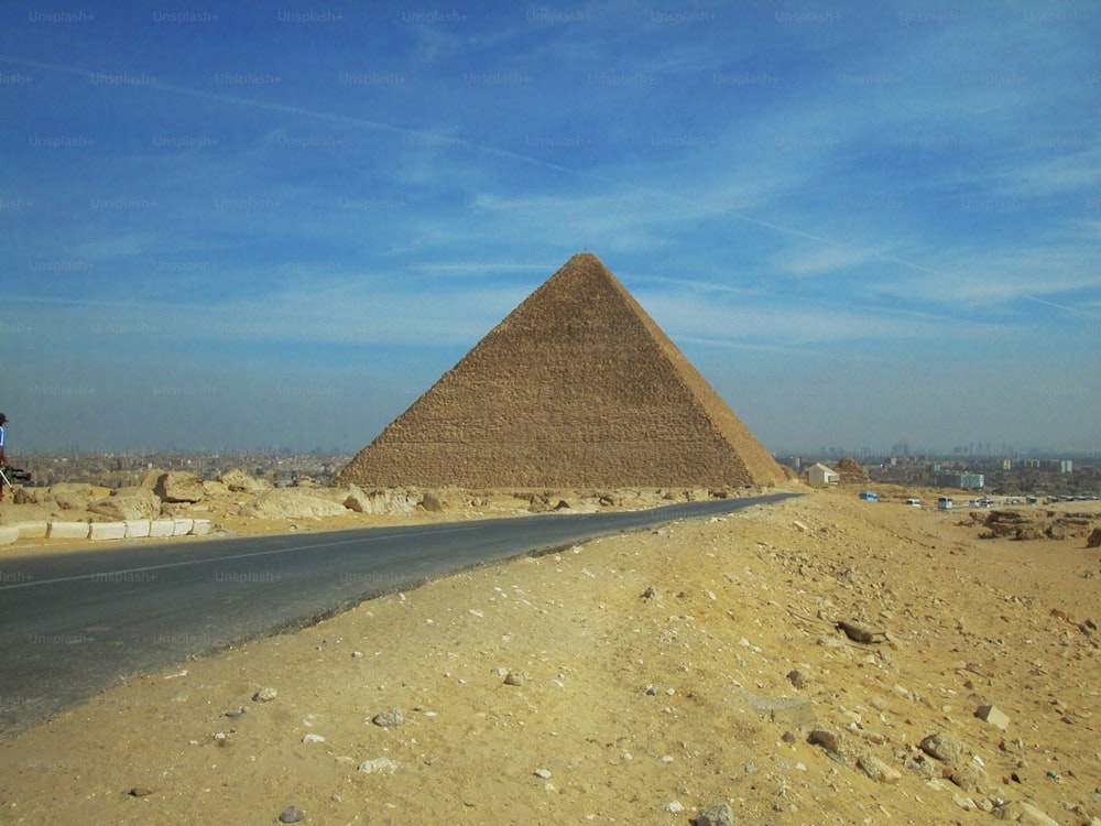 um homem andando de bicicleta por uma estrada ao lado de uma grande pirâmide