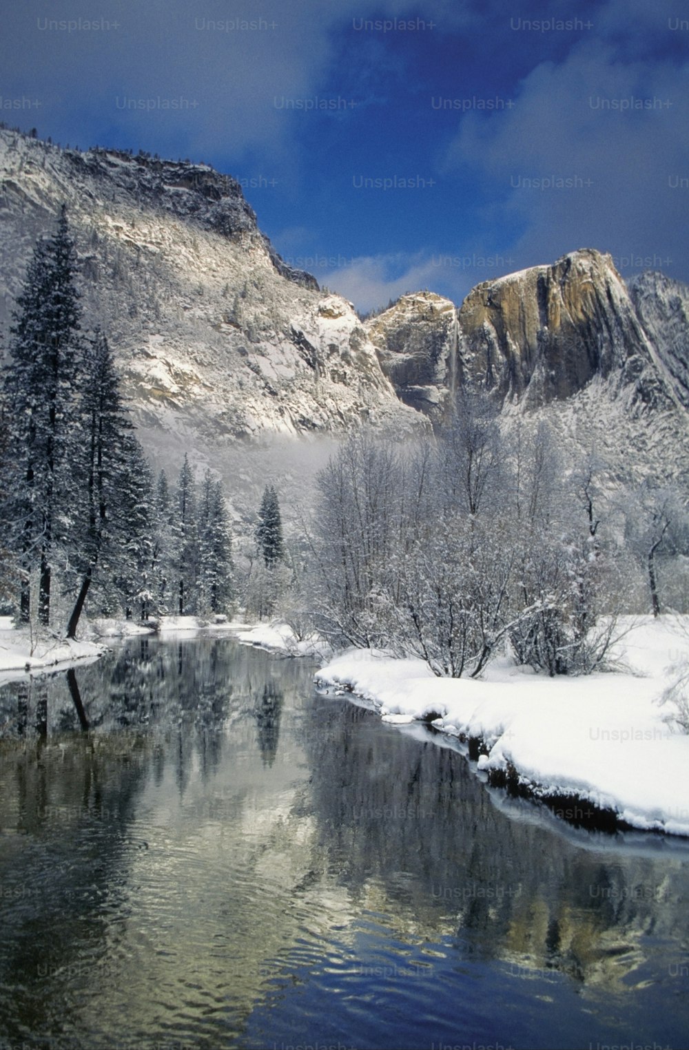 a river surrounded by snow covered mountains under a blue sky