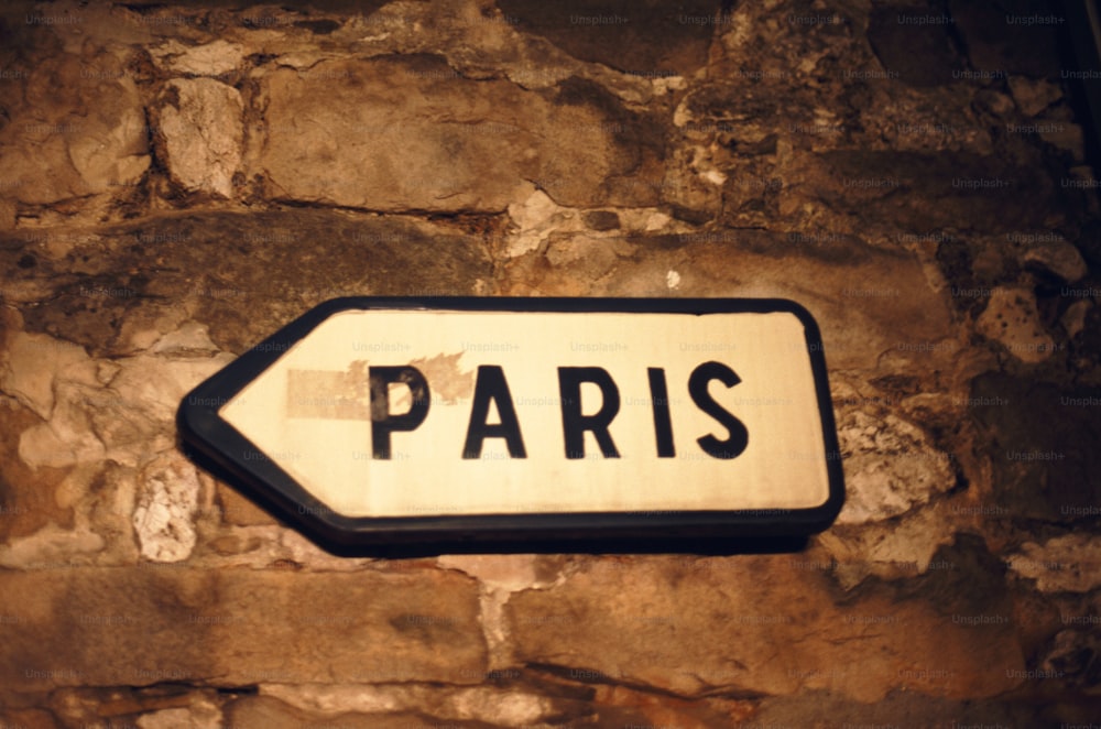 a white and black street sign on a stone wall