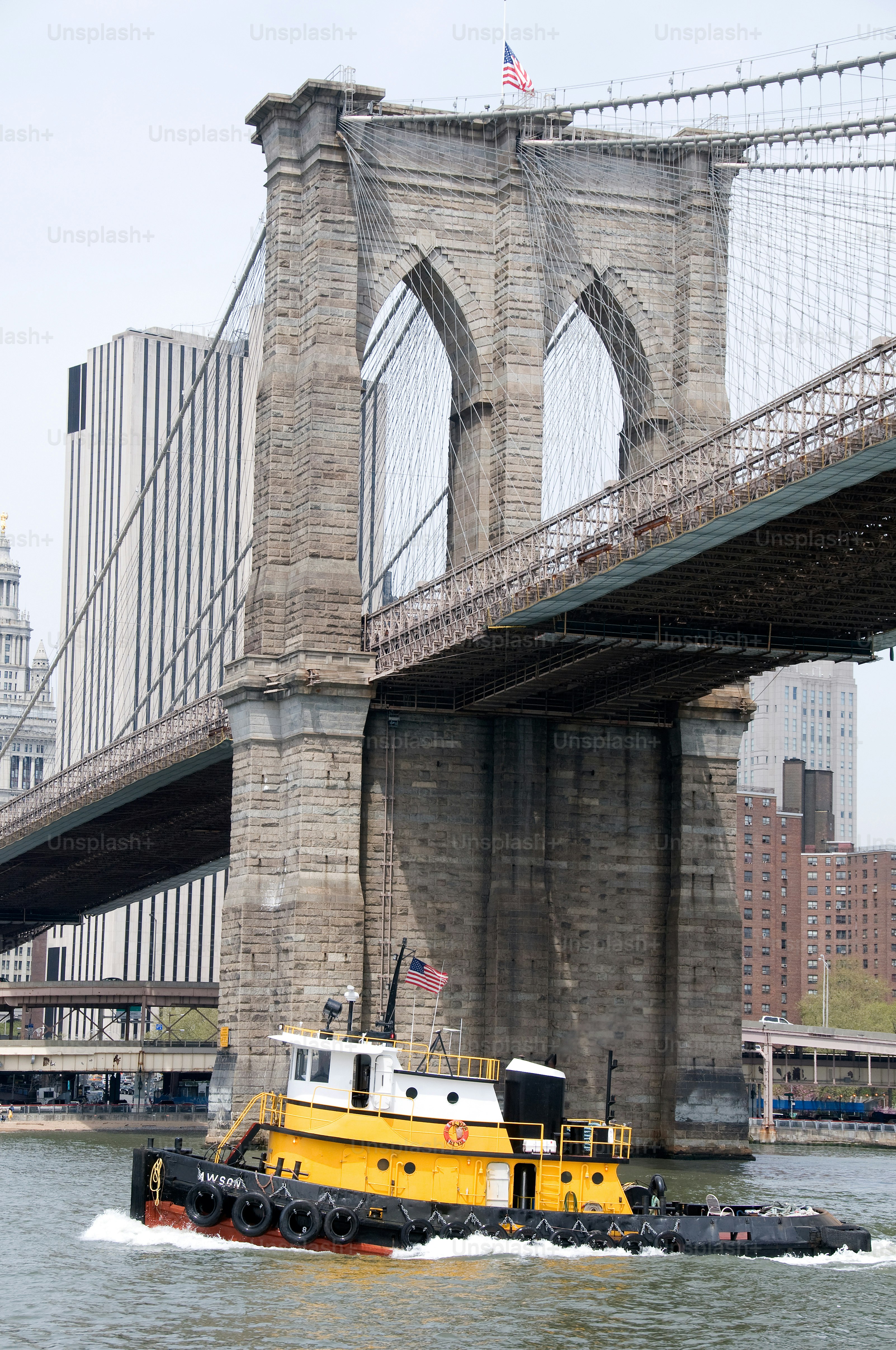 a yellow tug boat traveling under a bridge