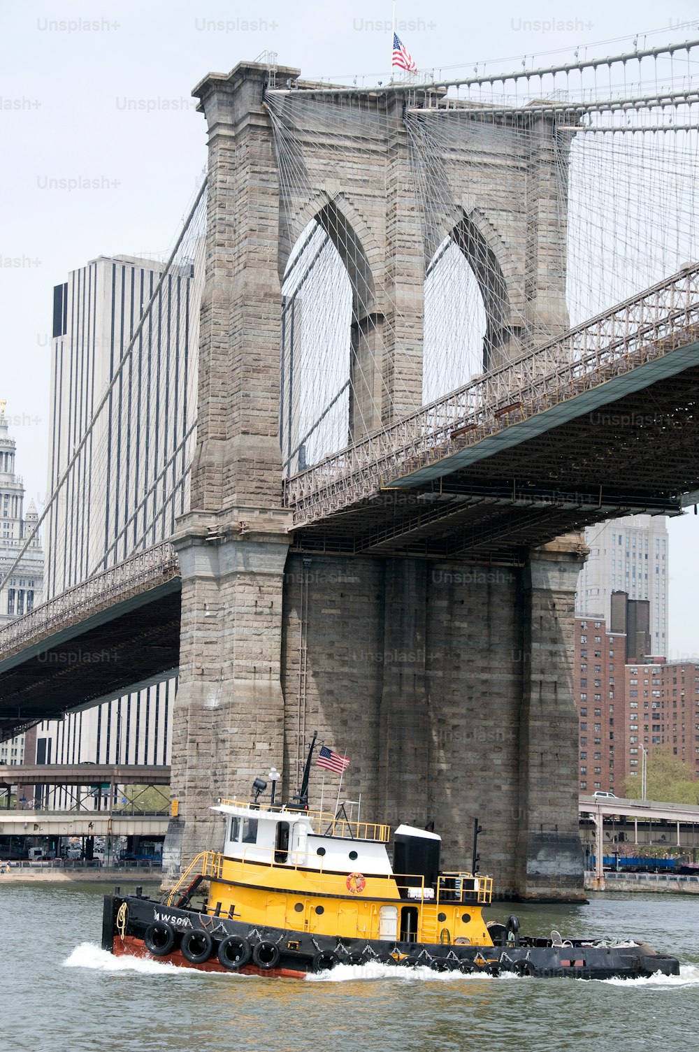 a yellow tug boat traveling under a bridge