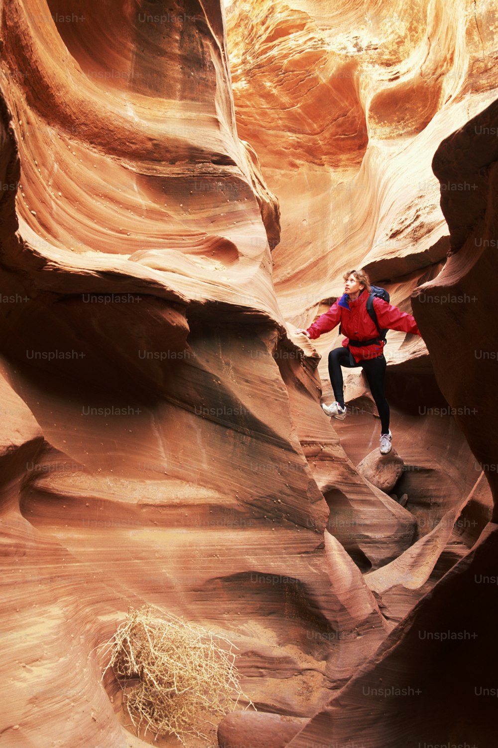 a man in a red jacket standing in a slot in a canyon