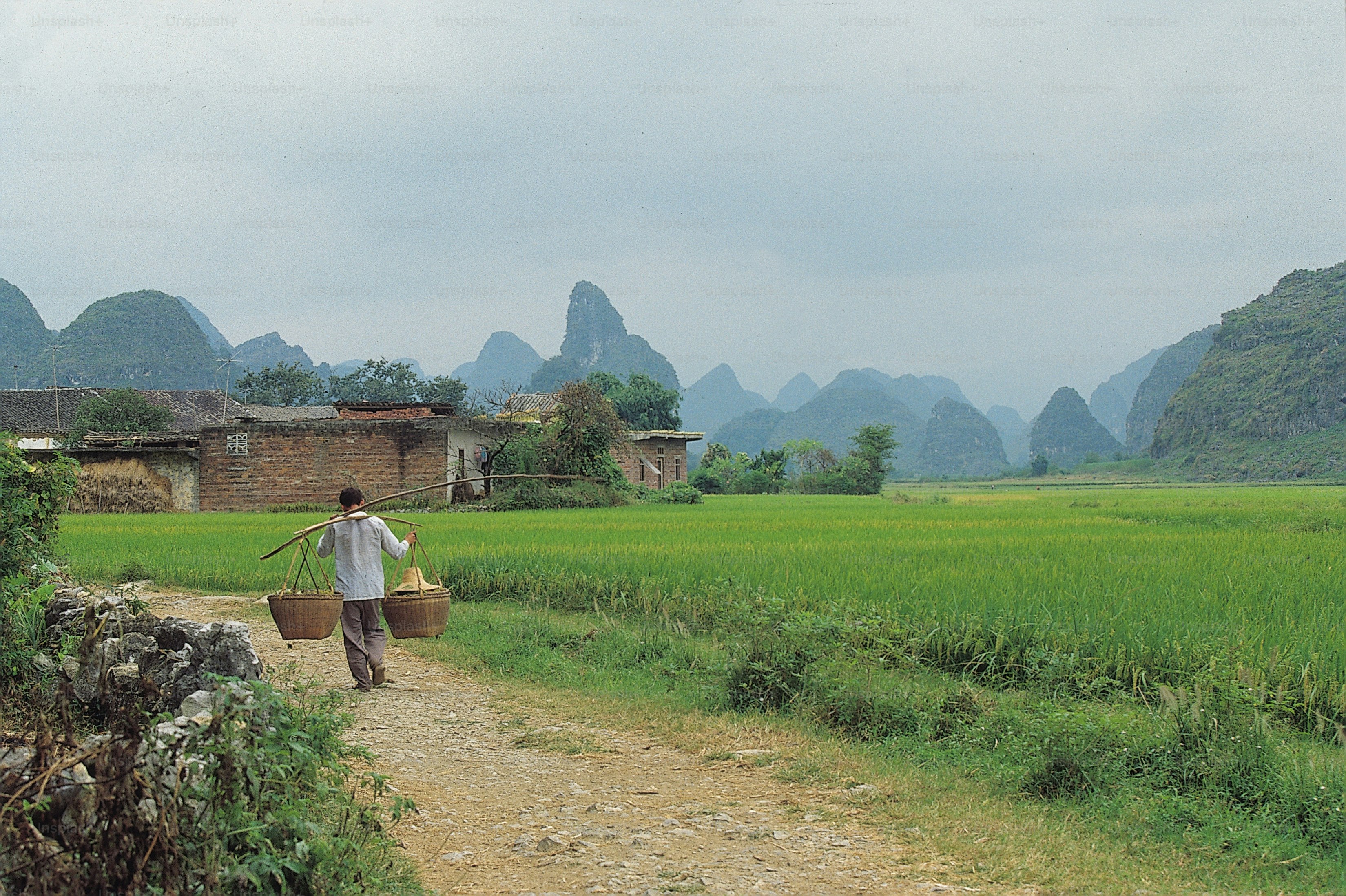 a man walking down a dirt road carrying a basket